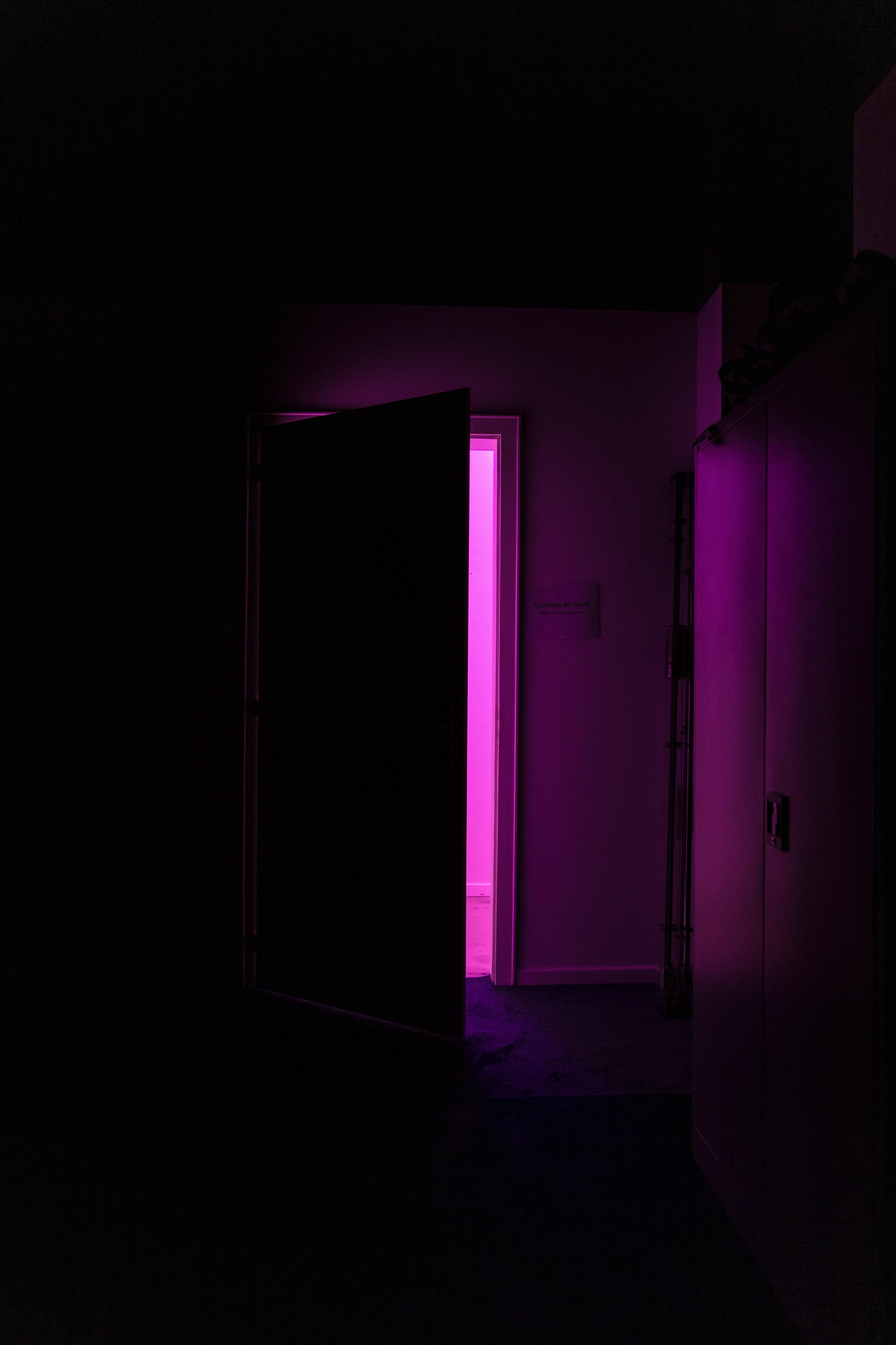 Neon Light 桌布 壁紙 — 一條黑暗的走廊，有一扇打開的門，露出從另一邊透出的鮮豔粉紅色光芒。