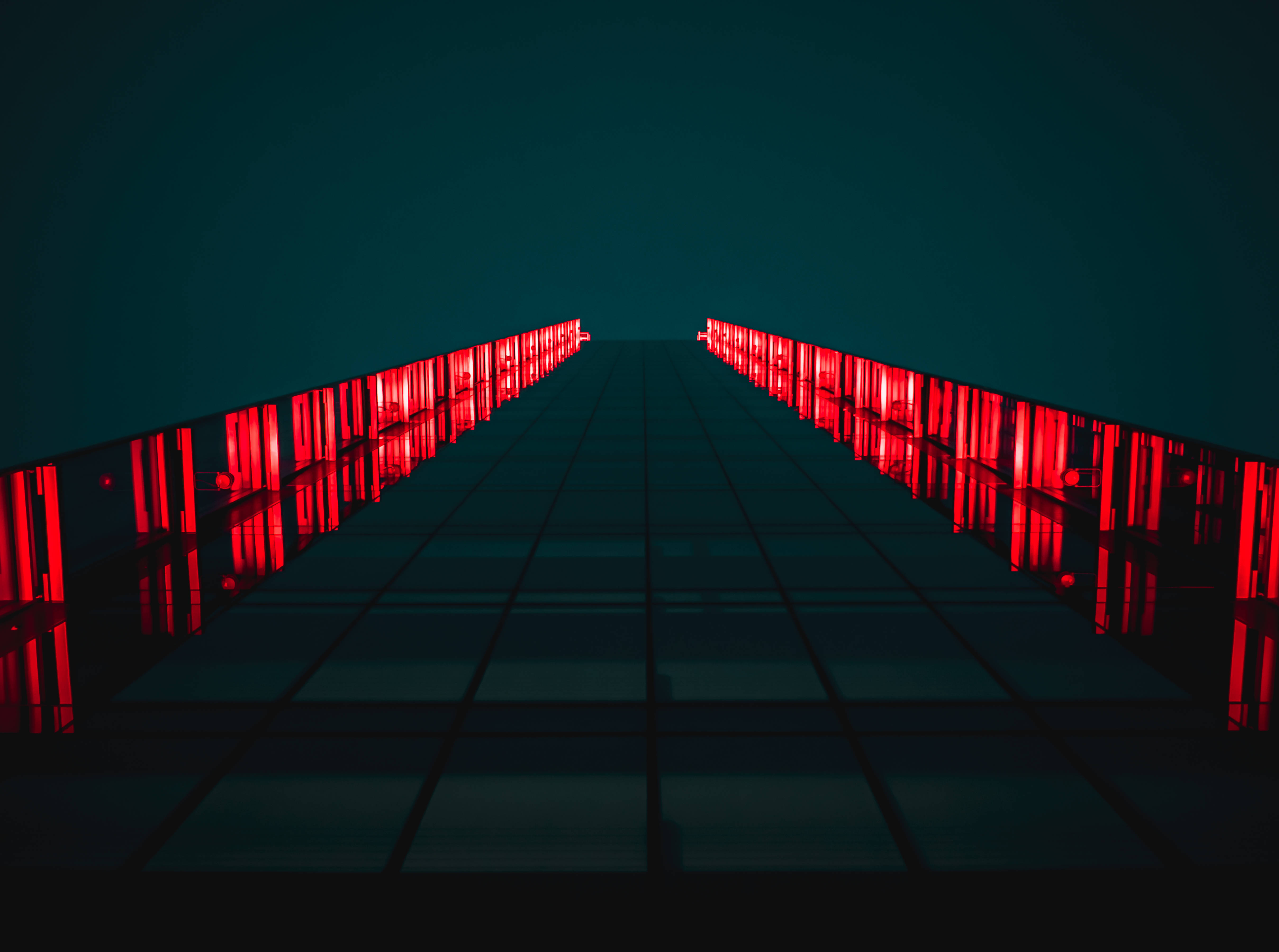 dark neon iPhone 桌布 壁紙 — 一條黑暗的隧道，兩側有發光的紅色垂直燈光，形成一條對稱的路徑，向遠方延伸。