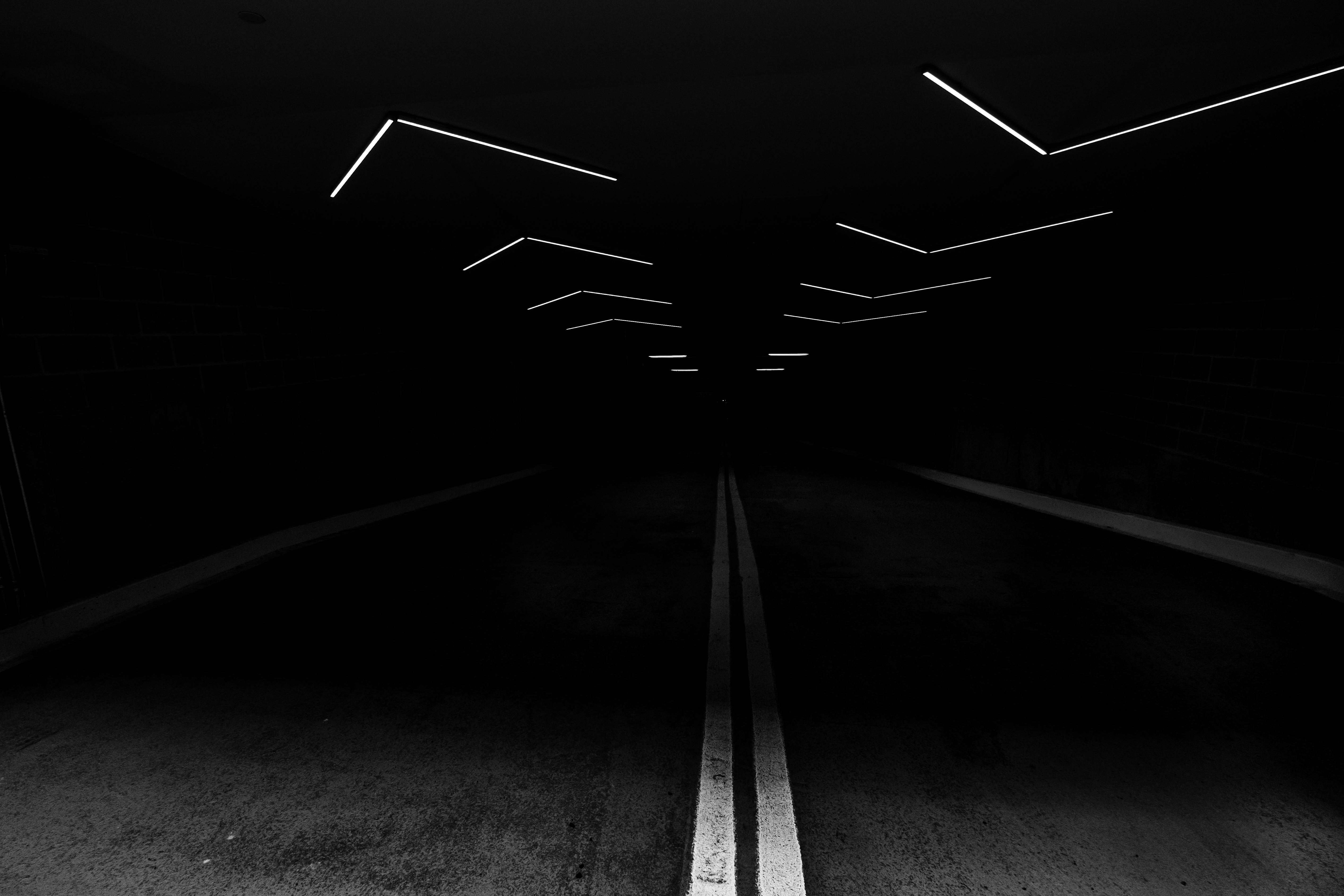 dark black 桌布 壁紙 — 一條黑暗的隧道，頭頂有發光的白色幾何燈光，中間的馬路線引向黑暗。