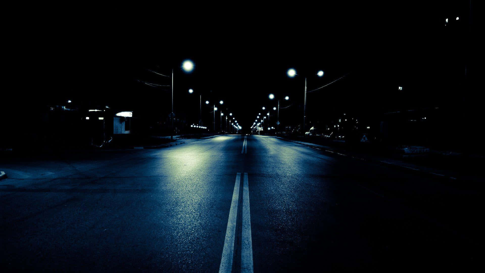 Road 桌布 壁紙 — 一條黑暗空曠的道路延伸入夜，遠處的路燈在濕瀝青上投射出藍色倒影。