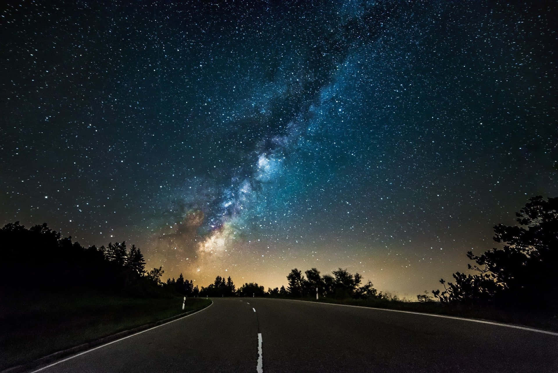 星星動圖 桌布 壁紙 — 一條黑暗蜿蜒的道路在令人嘆為觀止的星空下延伸，銀河系閃爍著鮮豔的藍色和白色。