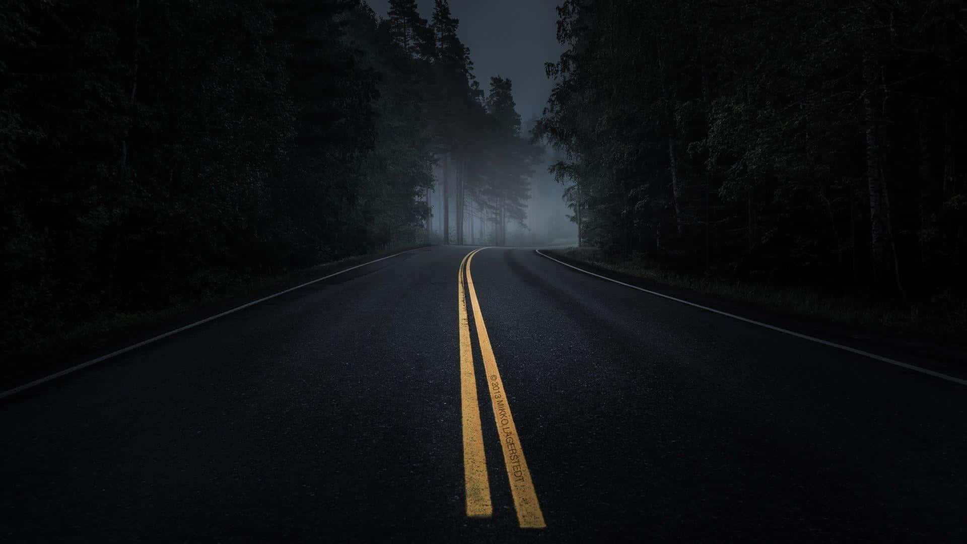 Road 桌布 壁紙 — 一條黑暗蜿蜒的道路在夜間穿過霧氣瀰漫的森林，發光的黃色中心線指引著方向。