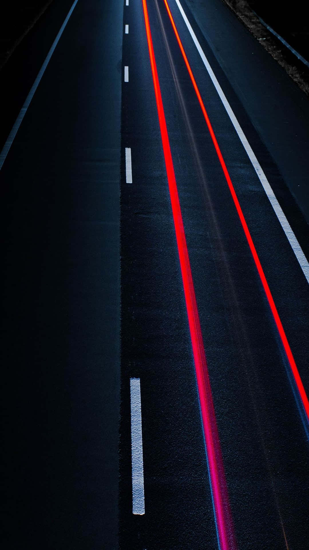 time lapse 桌布 壁紙 — 一條黑暗高速公路的長曝光照片，移動中的汽車留下鮮豔的紅色和藍色光軌，一直延伸到遠方。