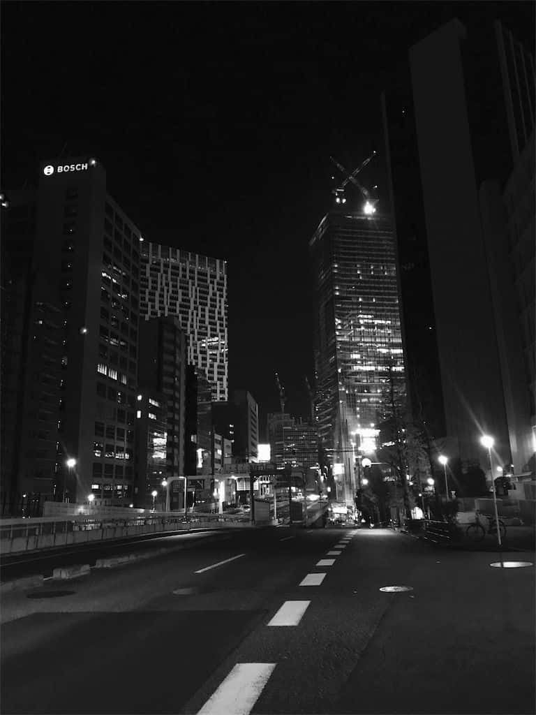 灰色美學動圖 桌布 壁紙 — 一條黑白夜景城市街道，兩旁是高聳的摩天大樓，窗戶亮著燈，街燈投下長長的影子。
