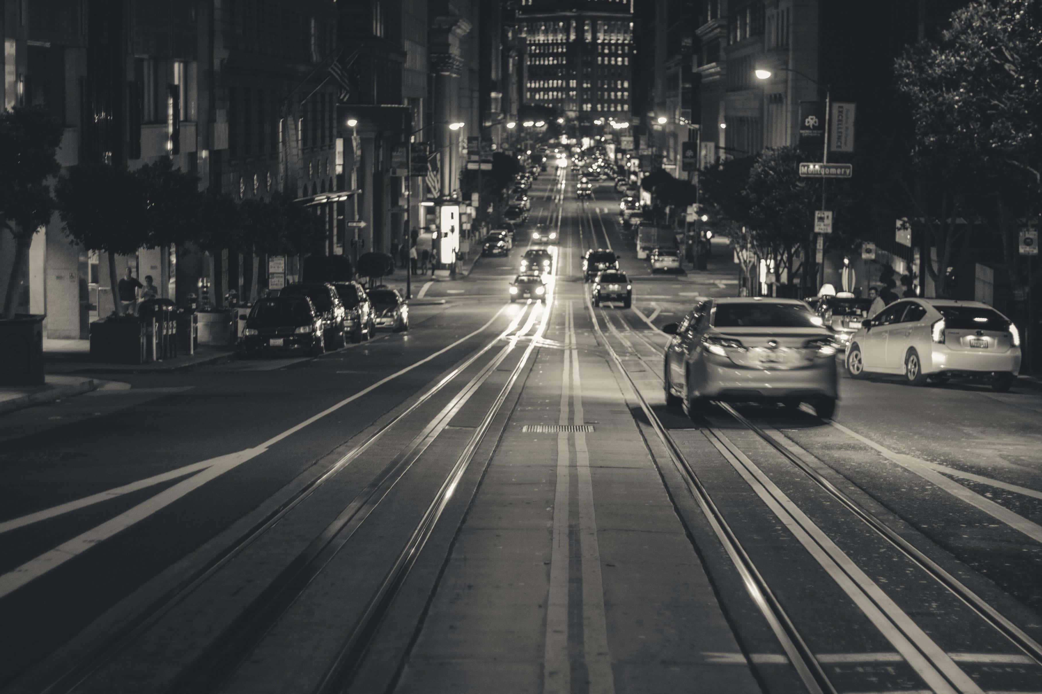 Black And White Street 桌布 壁紙 — 一條黑白夜景城市街道，汽車和街燈在電車軌道上投下長長的影子。