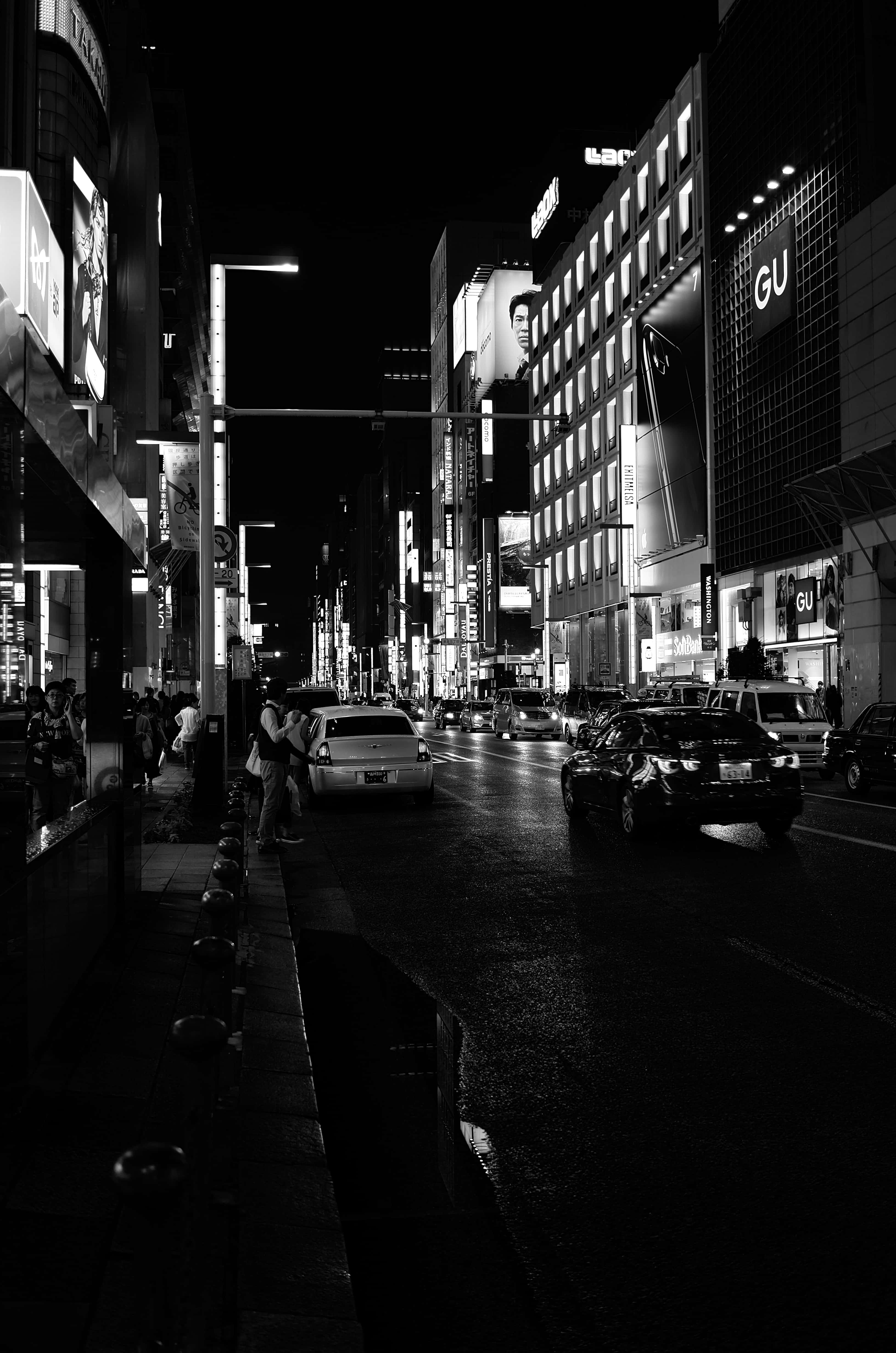手機 桌布 壁紙 — 一條黑白夜景城市街道，霓虹燈牌在濕漉漉的人行道上反射，汽車駛過。