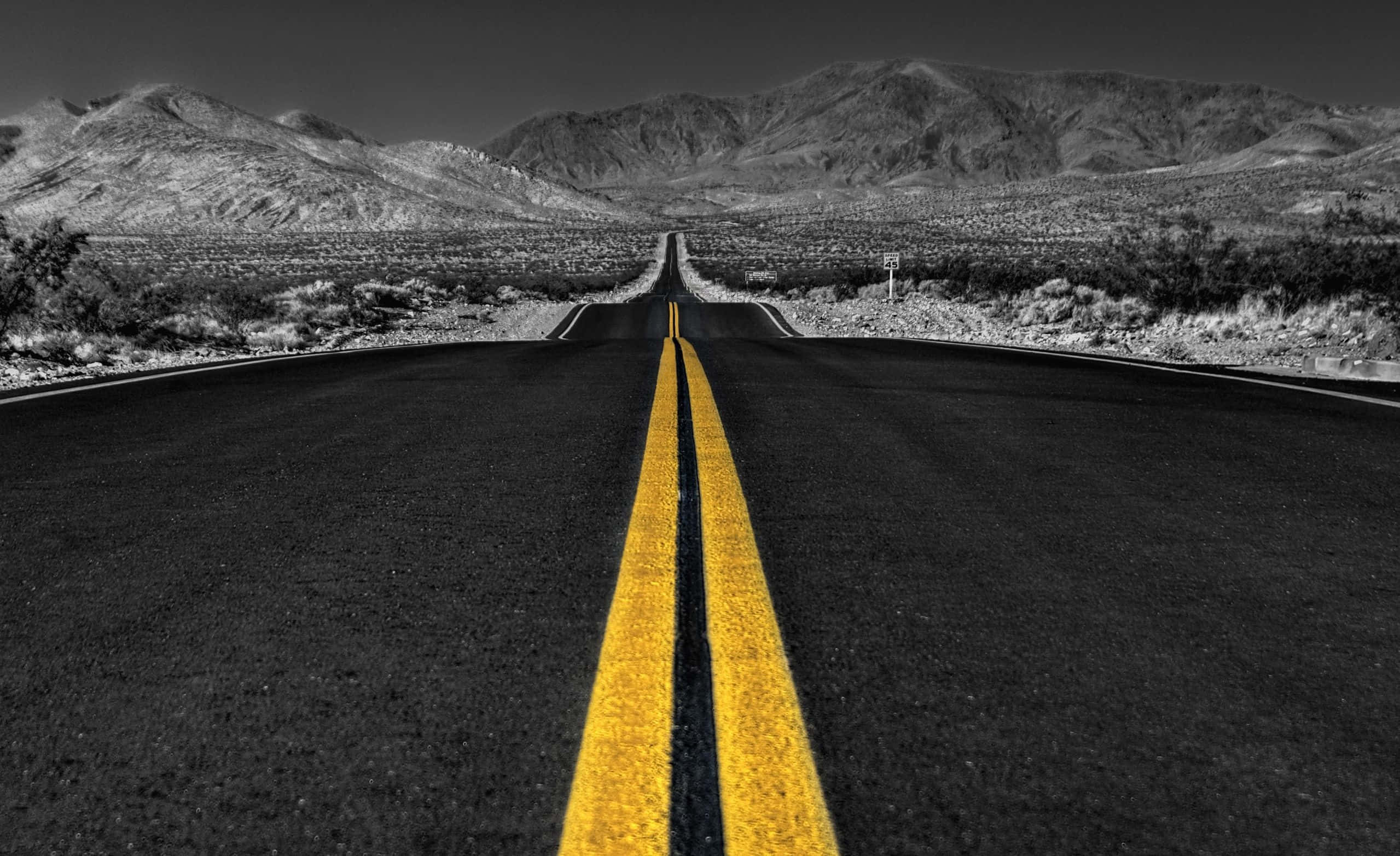Dark Road 桌布 壁紙 — 一條黑白沙漠公路伸向遠山，鮮黃色雙線引領前路。