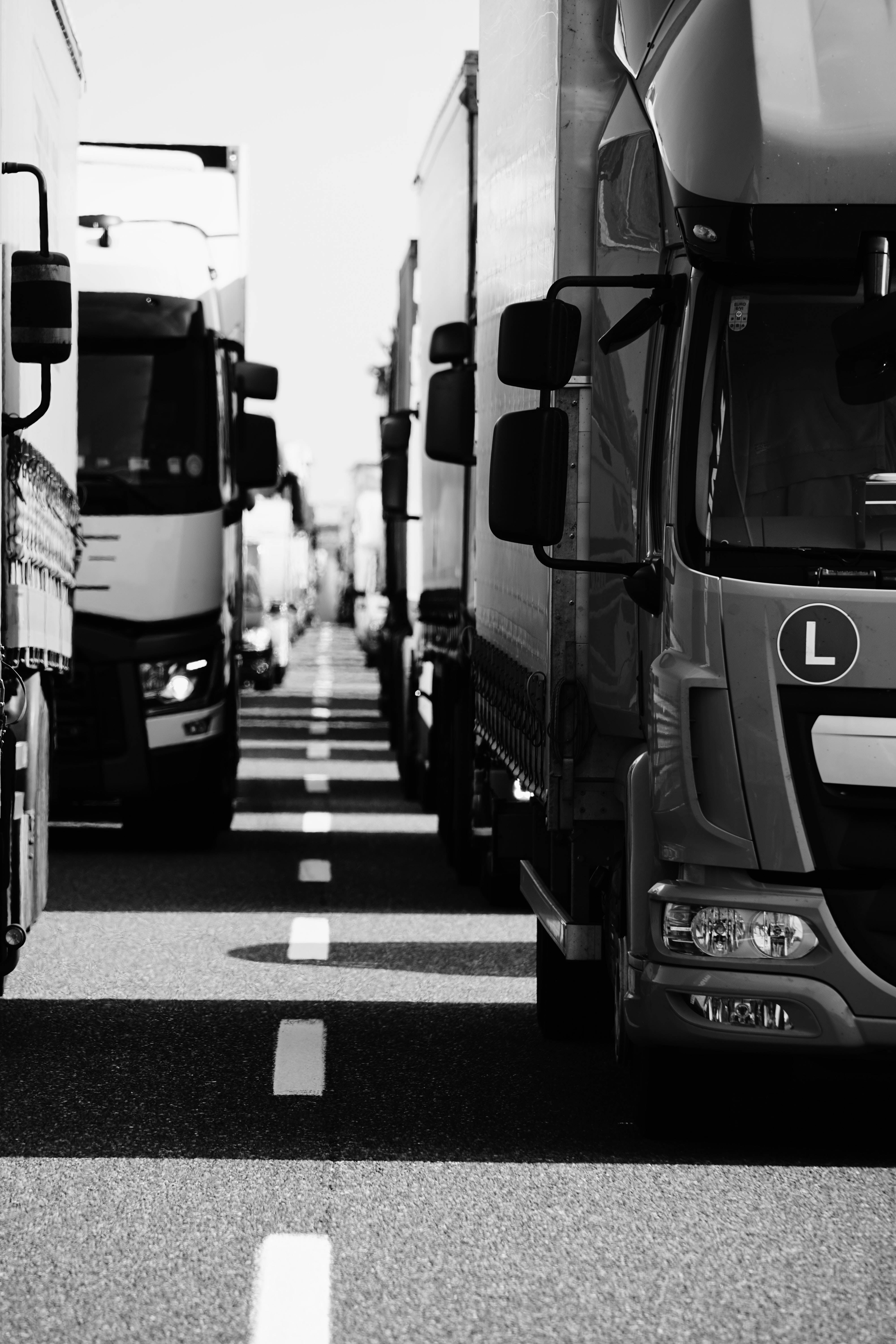 卡車 桌布 壁紙 — 一條黑白透視的道路，兩旁停滿了半掛卡車，形成一條由鉻和陰影組成的隧道。