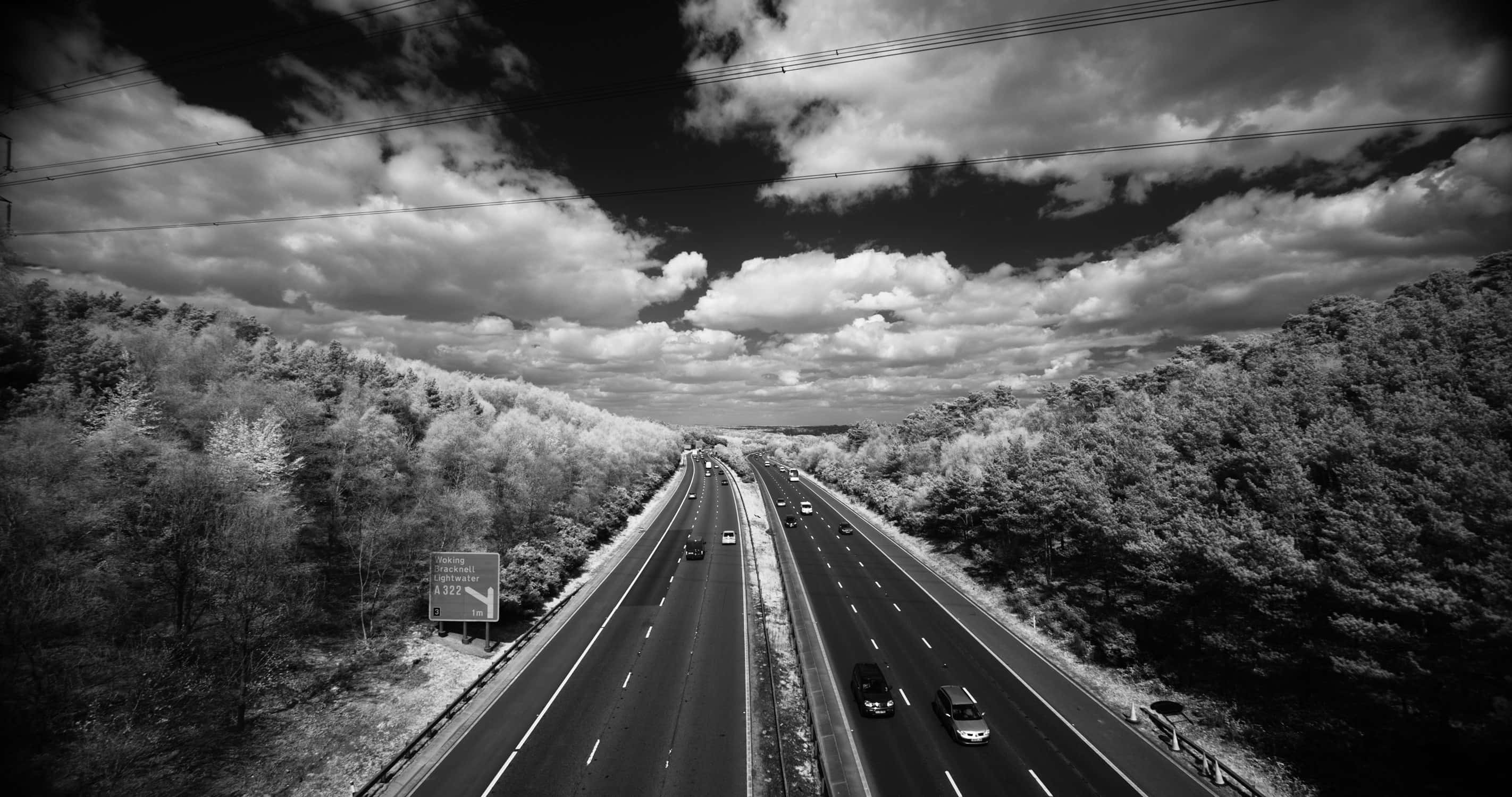 Monochrome 桌布 壁紙 — 一條黑白高速公路穿過茂密的森林，天空戲劇性地多雲，車輛雙向行駛。