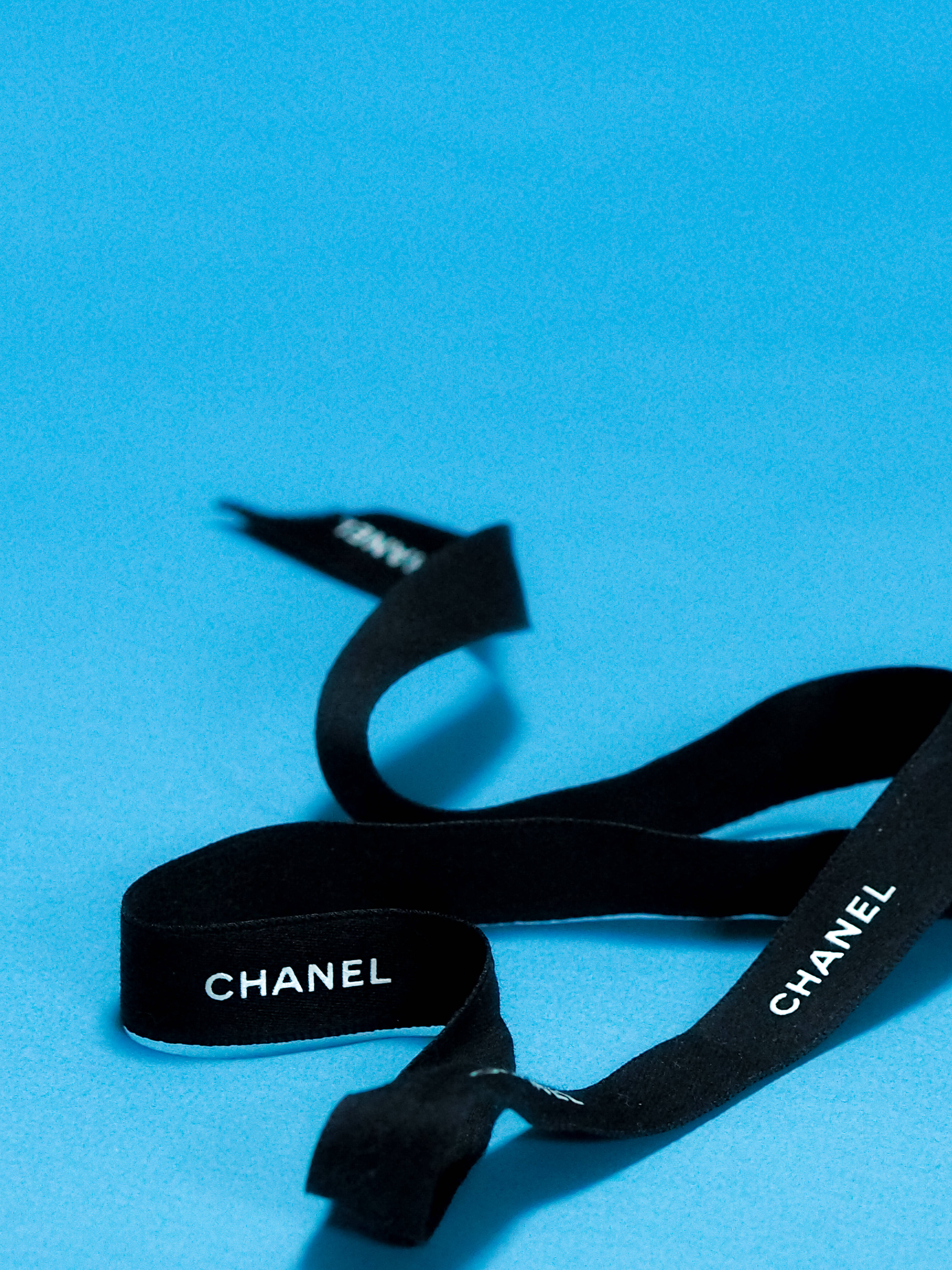 Chanel 桌布 壁紙 — 一條黑色Chanel絲帶，帶有白色字體，在純藍色背景上優雅地彎曲。