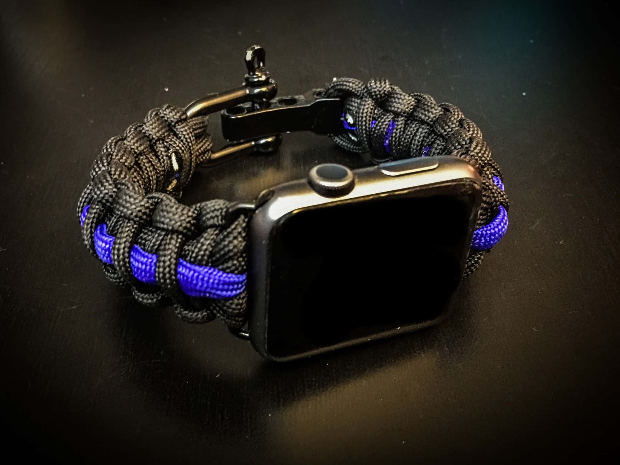 黑色Apple Watch配藍色傘繩錶帶在黑暗表面上 — 細藍線動圖 壁紙