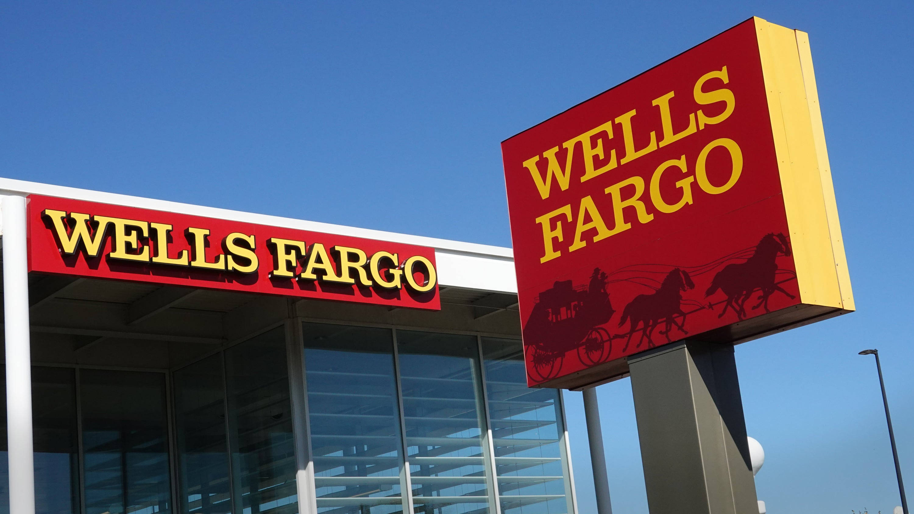 sign 桌布 壁紙 — 一棟 Wells Fargo 銀行建築，帶有紅色和黃色的標牌，上面有馬車標誌，背景是晴朗的藍天。