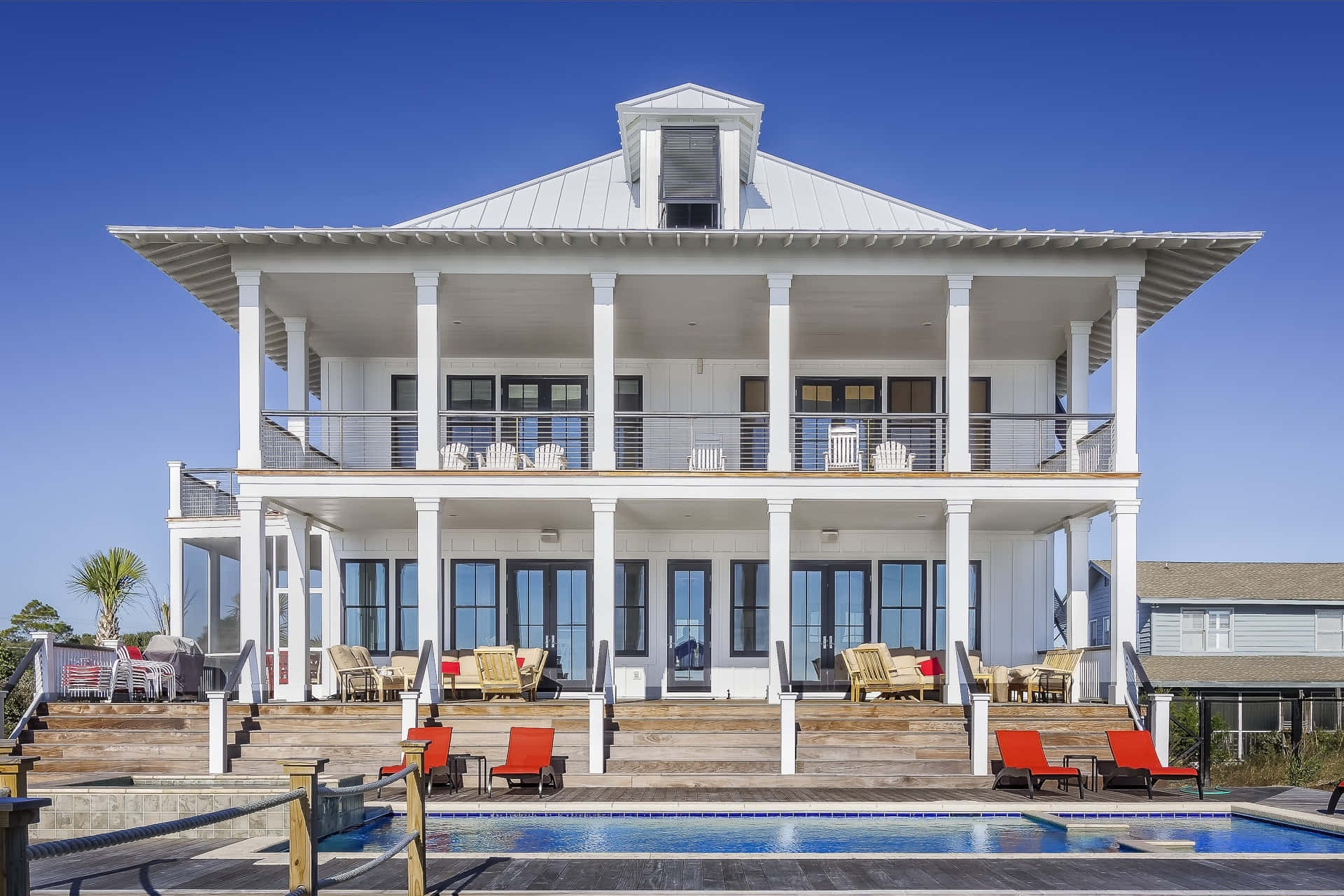 Luxury House 桌布 壁紙 — 一棟大型白色海灘別墅，設有環繞式門廊，俯瞰著清澈藍天下閃閃發光的游泳池。