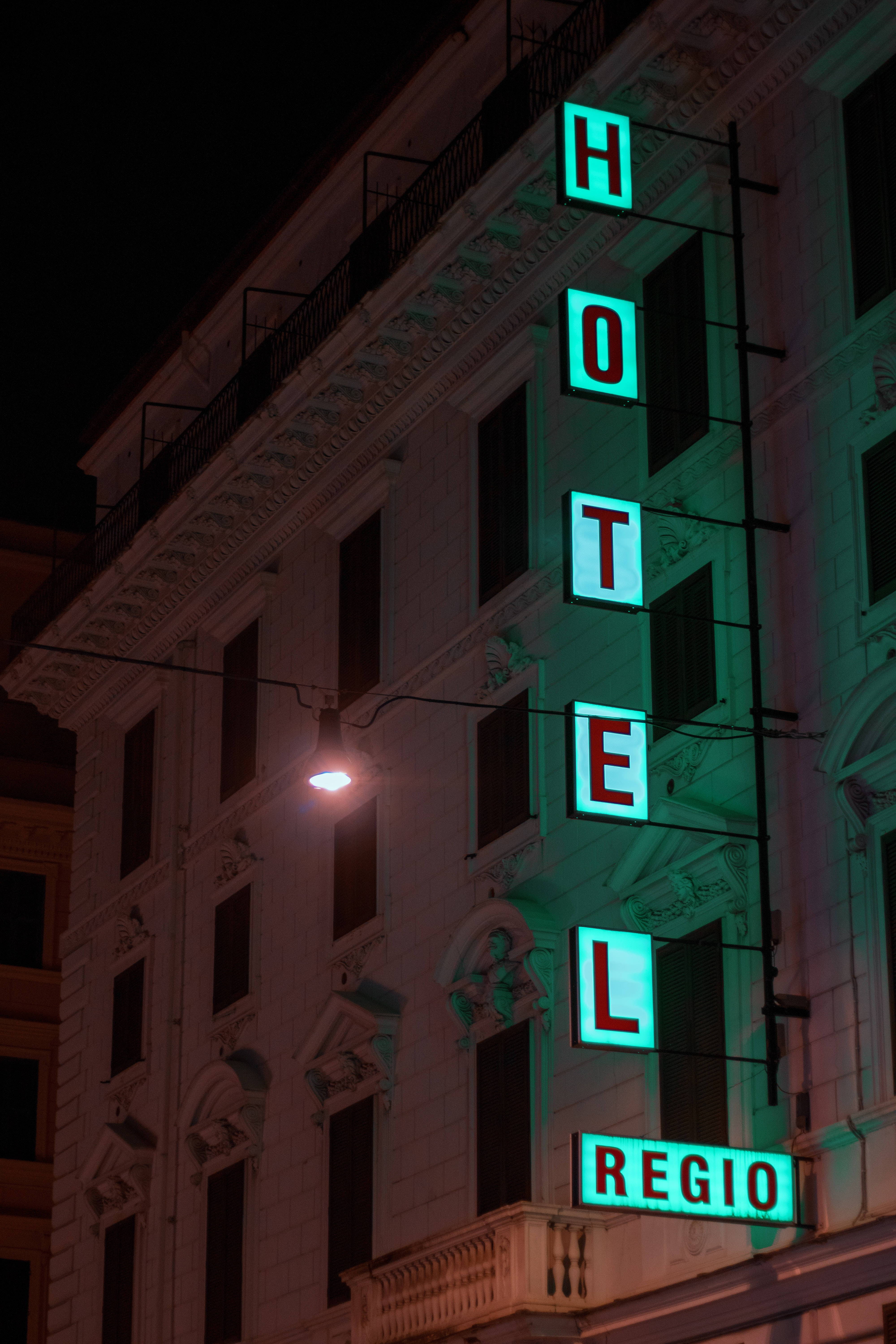Hotel 桌布 壁紙 — 一棟復古飯店建築在夜晚被發光的綠色霓虹燈招牌照亮，招牌上拼寫著「HOTEL REGIO」，背景是黑暗的天空。