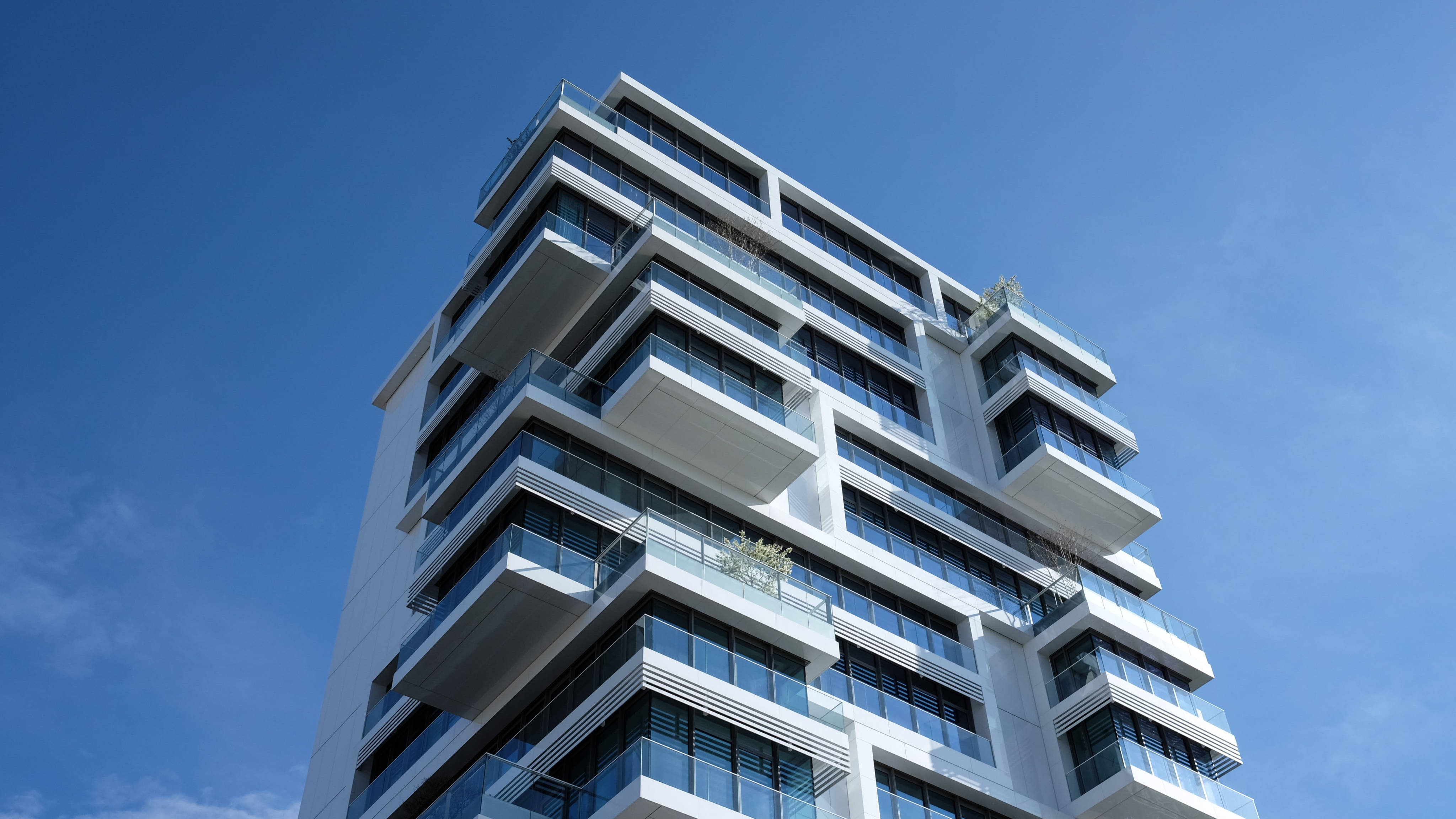 Building 桌布 壁紙 — 一棟現代白色高層公寓大樓，帶有玻璃陽台，聳立在清澈的藍天下。