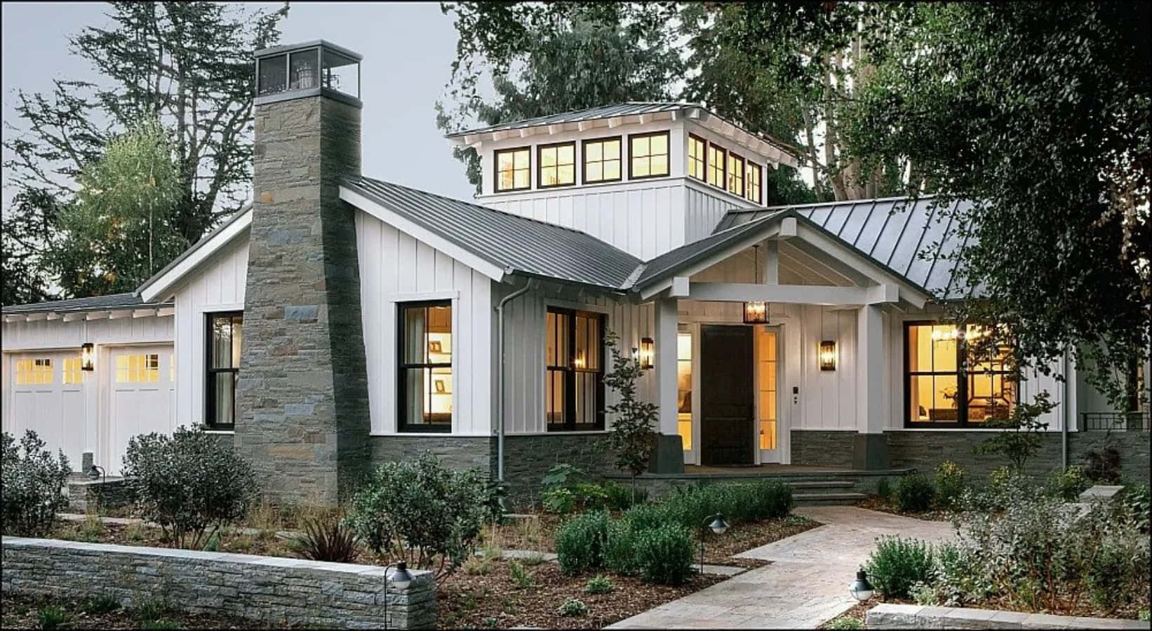 Modern Farmhouse 桌布 壁紙 — 一棟現代農舍，白色牆板搭配石材點綴，在黃昏時分被茂密綠植環繞，散發溫暖光芒。