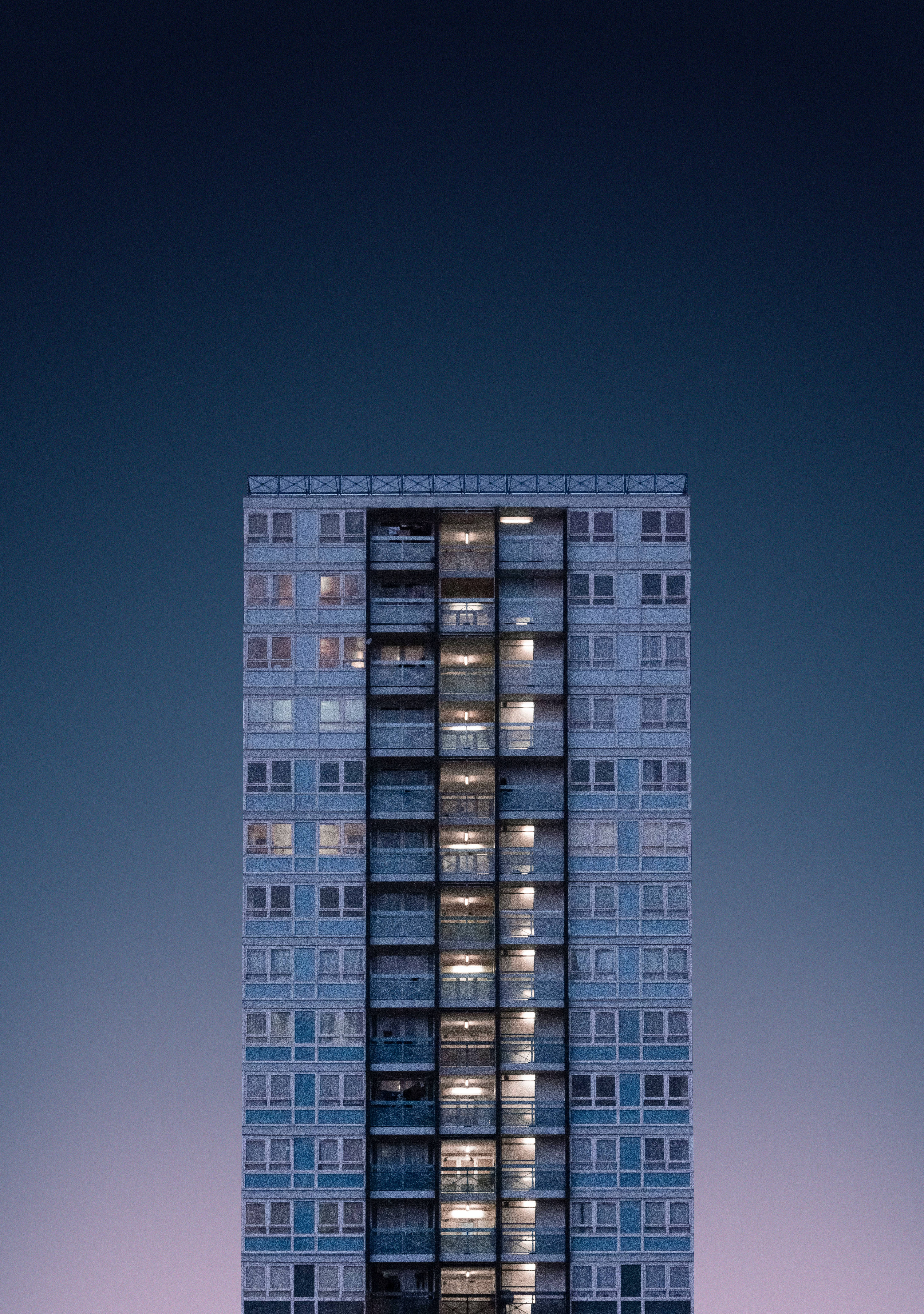 極簡動態 桌布 壁紙 — 一棟高層公寓大樓矗立在暮色天空下，窗戶透出溫暖的燈光。