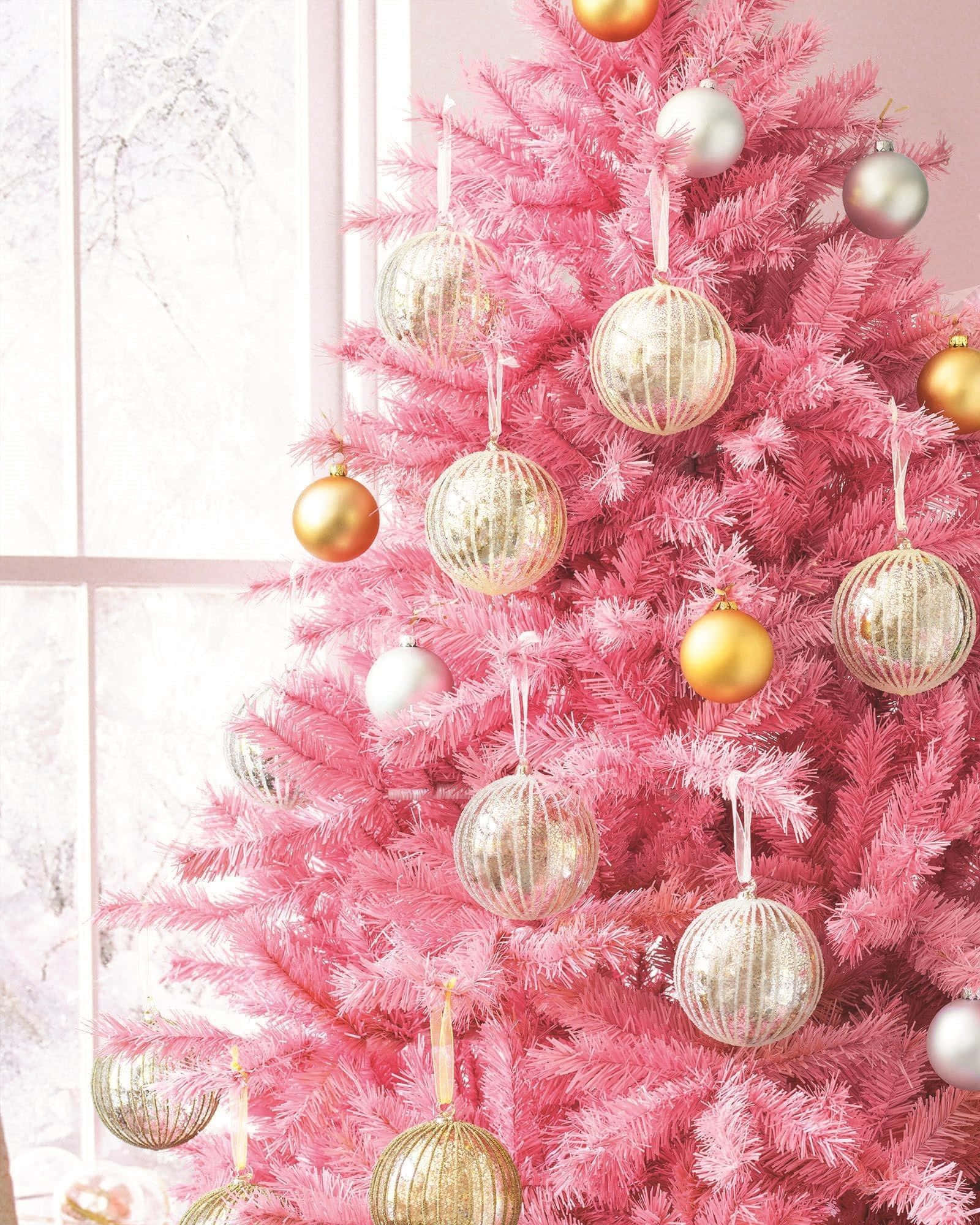 Rose Gold Christmas 桌布 壁紙 — 一棵充滿活力的粉紅色聖誕樹，裝飾著閃閃發光的金色和銀色飾品，矗立在積雪的窗邊。