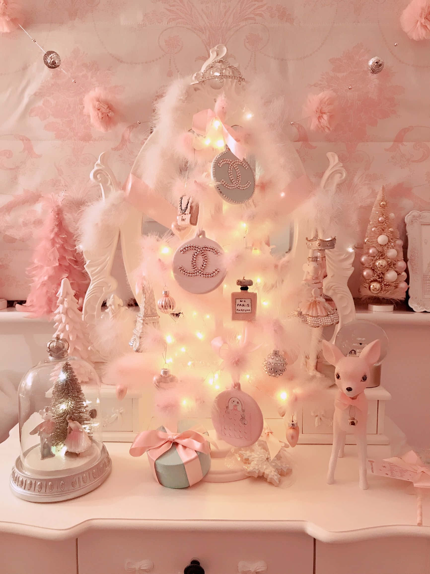 Pink Christmas Tree 桌布 壁紙 — 一棵夢幻的粉紅色聖誕樹，裝飾著Chanel飾品和仙女燈，在相配的梳妝檯上柔和地發光。