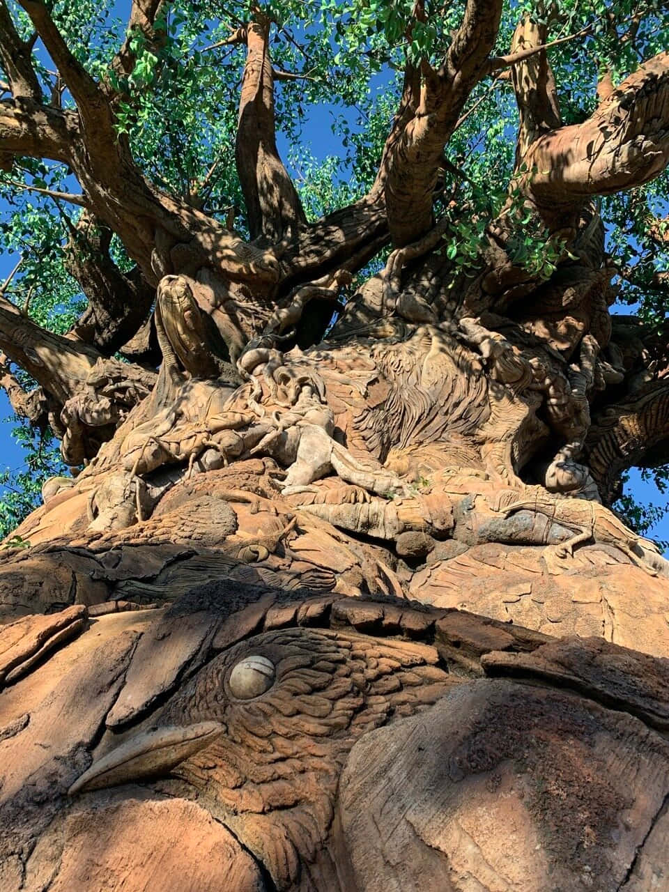 Tree Of Life 桌布 壁紙 — 一棵巨大而雕刻精細的樹木，樹幹中嵌有動物圖案，映襯著清澈的藍天。