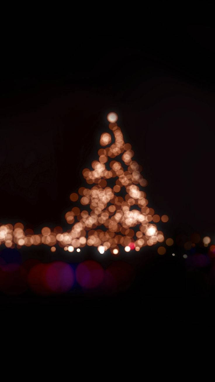Christmas Lights Aesthetic 桌布 壁紙 — 一棵散景聖誕樹，在漆黑的夜空下閃爍著溫暖的金色光芒。