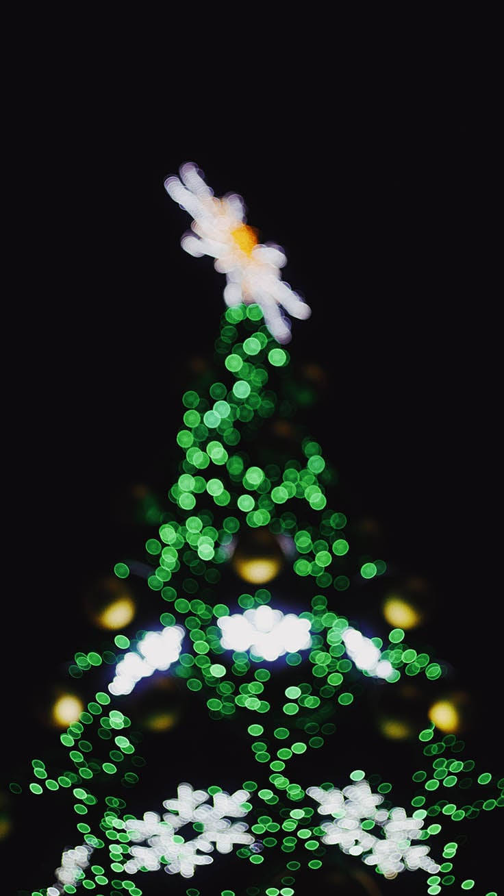 Christmas Lights Aesthetic 桌布 壁紙 — 一棵散景聖誕樹，帶有綠色燈光和白色雪花裝飾，襯托著黑暗的夜空。