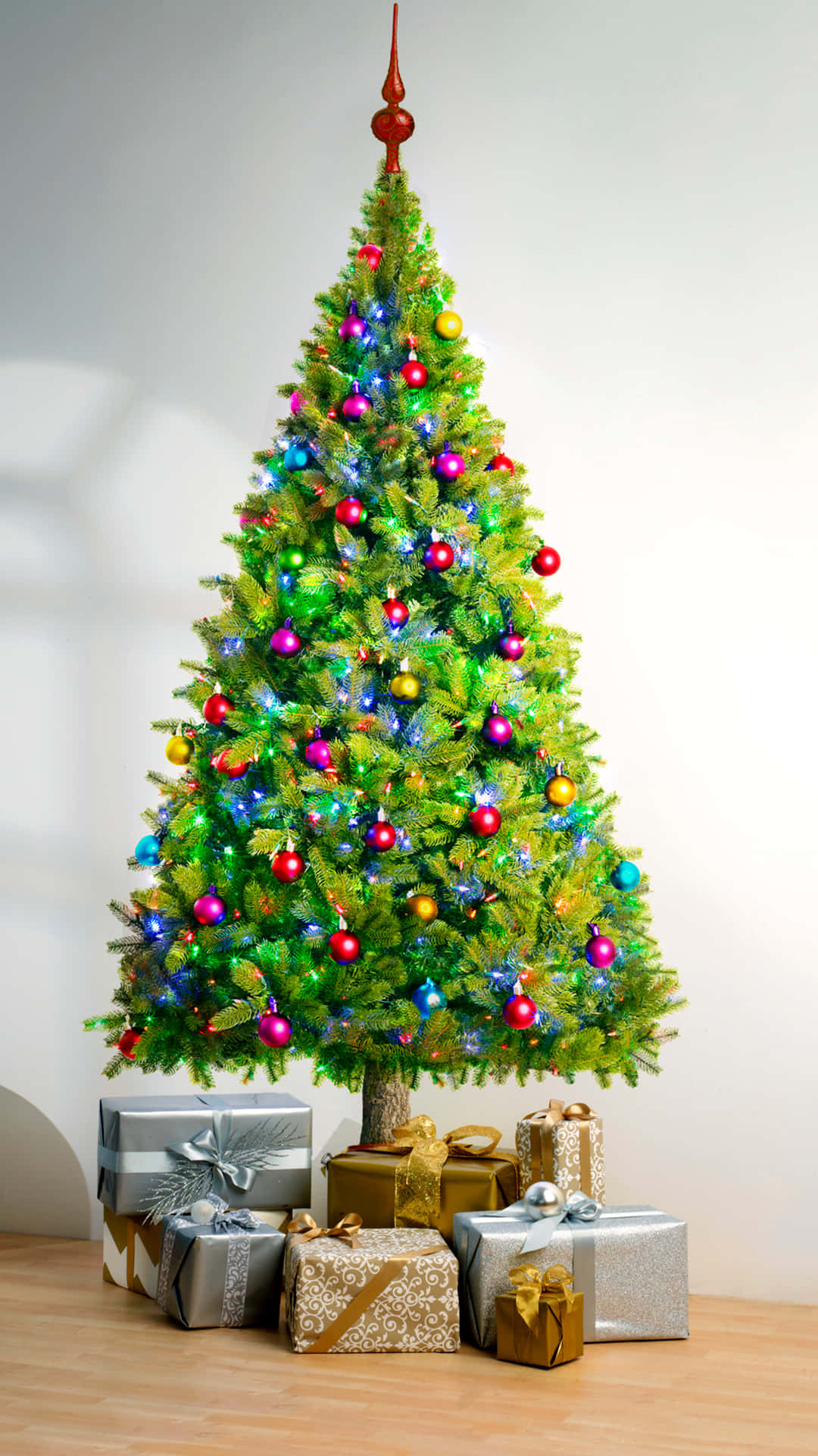 Cute Christmas Tree 桌布 壁紙 — 一棵明亮照亮的聖誕樹，裝飾著色彩繽紛的飾物和閃爍的燈光，周圍是木地板上包裝好的禮物。