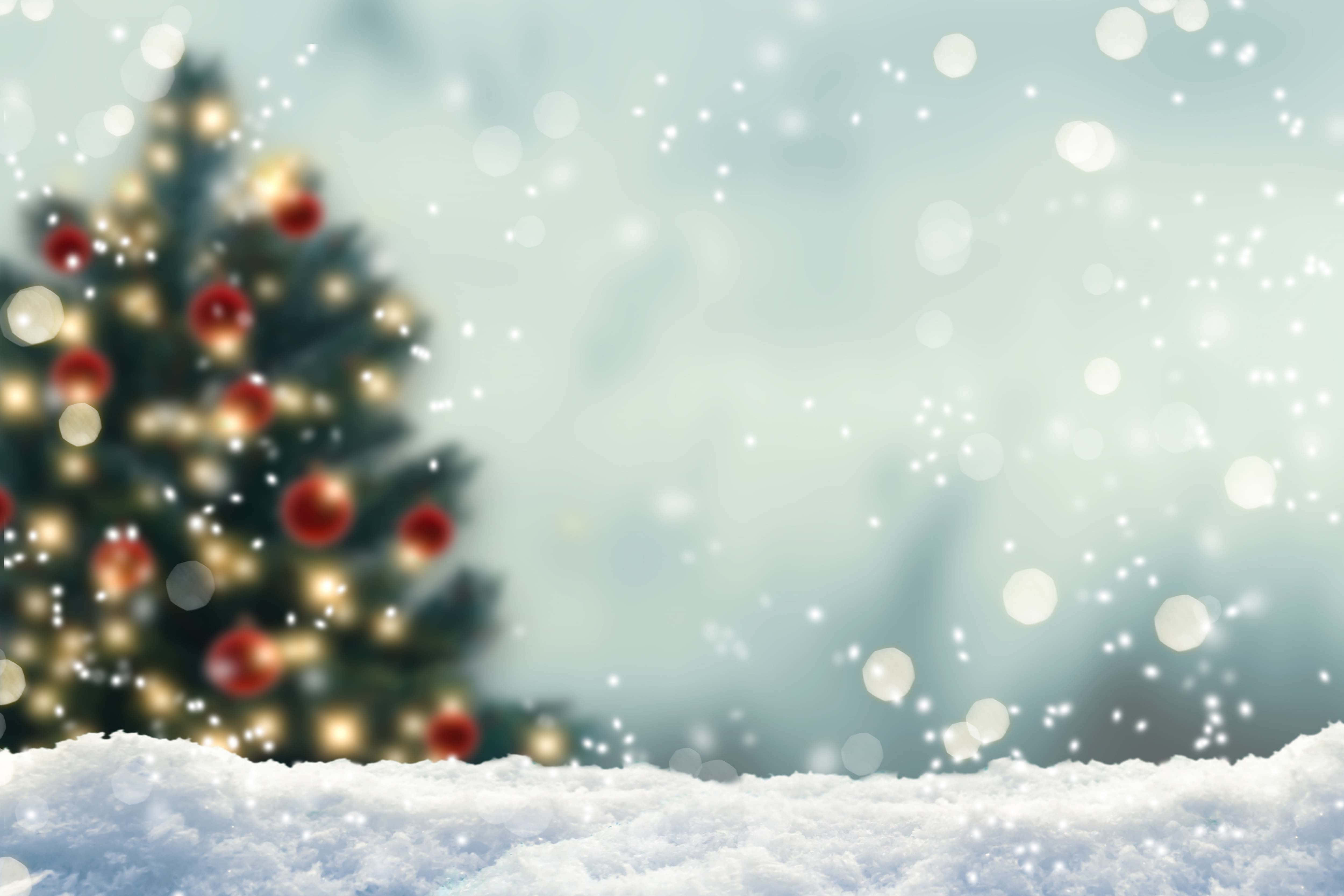 Microsoft Teams Christmas 桌布 壁紙 — 一棵柔和模糊的聖誕樹，裝飾著紅色飾品和溫暖的燈光，矗立在雪白的冬日場景中，飄落的雪花和散景效果。