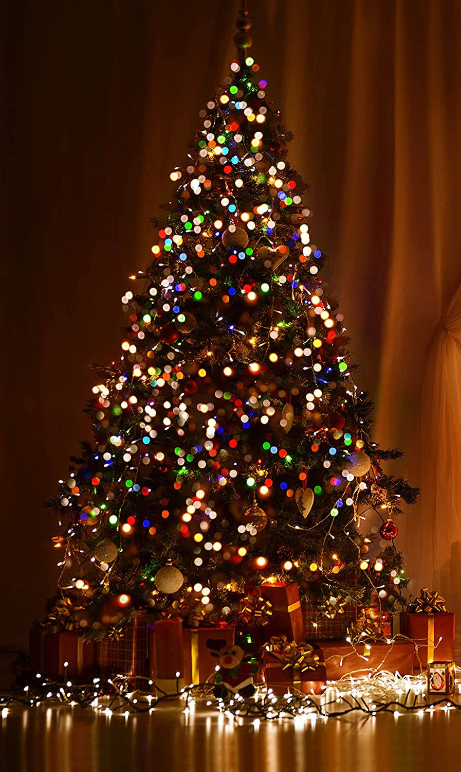 Christmas Lights Aesthetic 桌布 壁紙 — 一棵溫暖照明的聖誕樹，裝飾著彩色燈光和飾品，在柔和的金色光芒下與包裝好的禮物並肩而立。