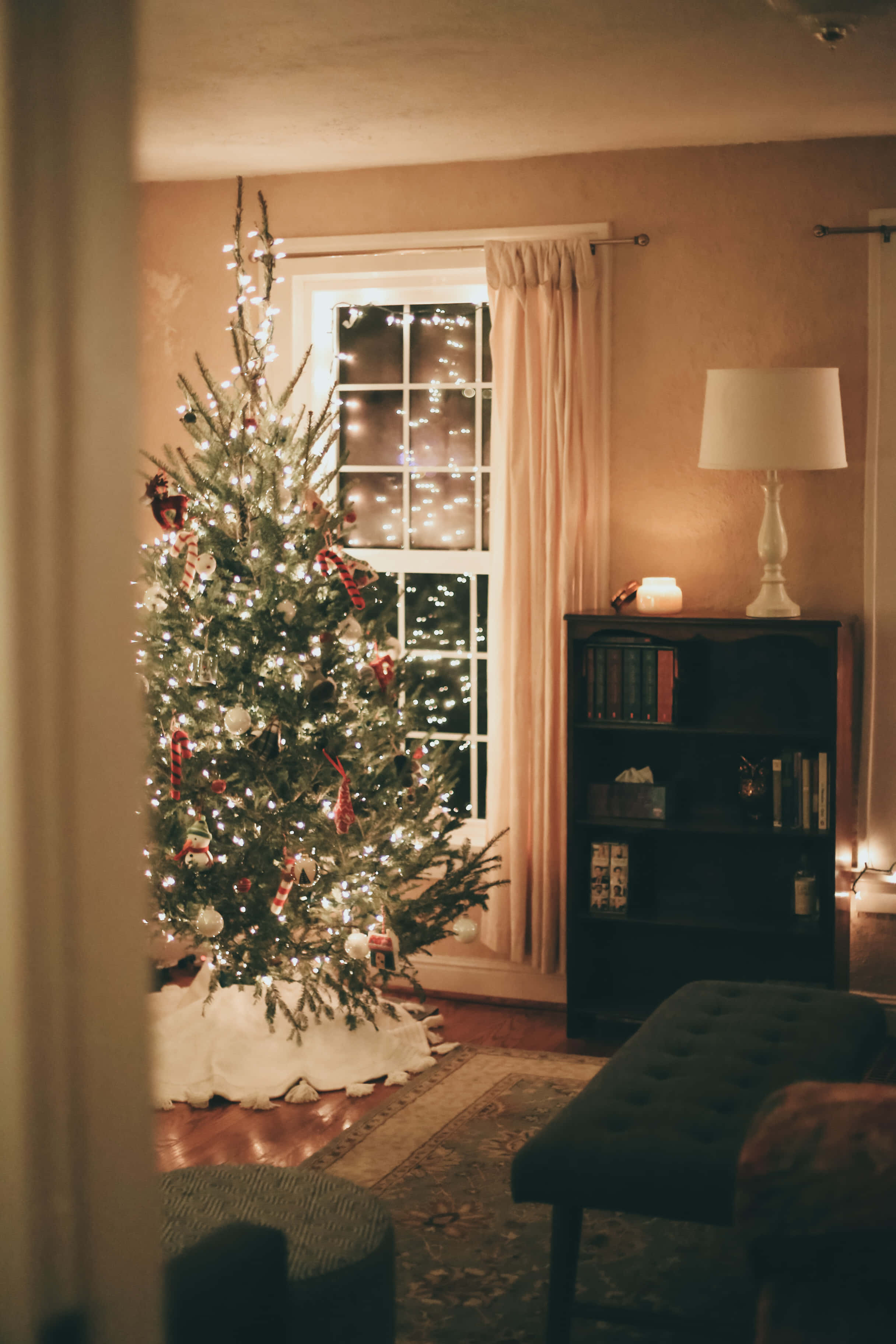 Christmas Living Room 桌布 壁紙 — 一棵溫暖照明的聖誕樹，裝飾著燈飾和糖果手杖飾品，放在一個舒適的客廳裡，靠近有窗簾的窗戶。