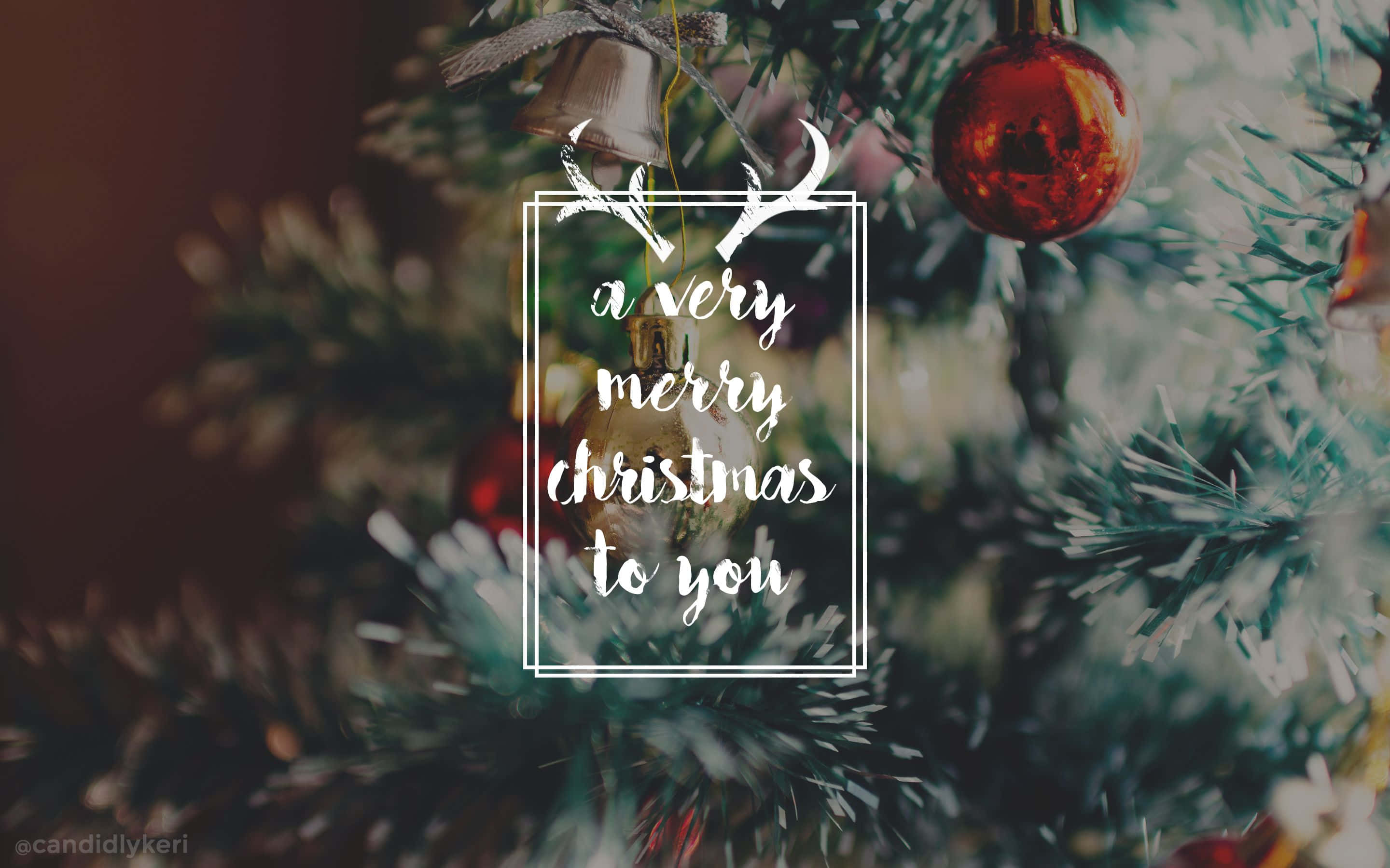Christmas Aesthetic Desktop 桌布 壁紙 — 一棵節日聖誕樹，裝飾著紅色飾品和一個鈴鐺，帶有白色框架的文字 'a very merry christmas to you' 和鹿角裝飾。