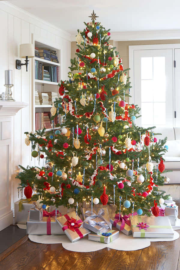 Aesthetic Christmas Tree 桌布 壁紙 — 一棵裝飾華麗的聖誕樹，掛滿紅、白、藍色的飾物和閃爍的燈光，高高矗立在舒適的客廳中，周圍環繞著包裝好的禮物。