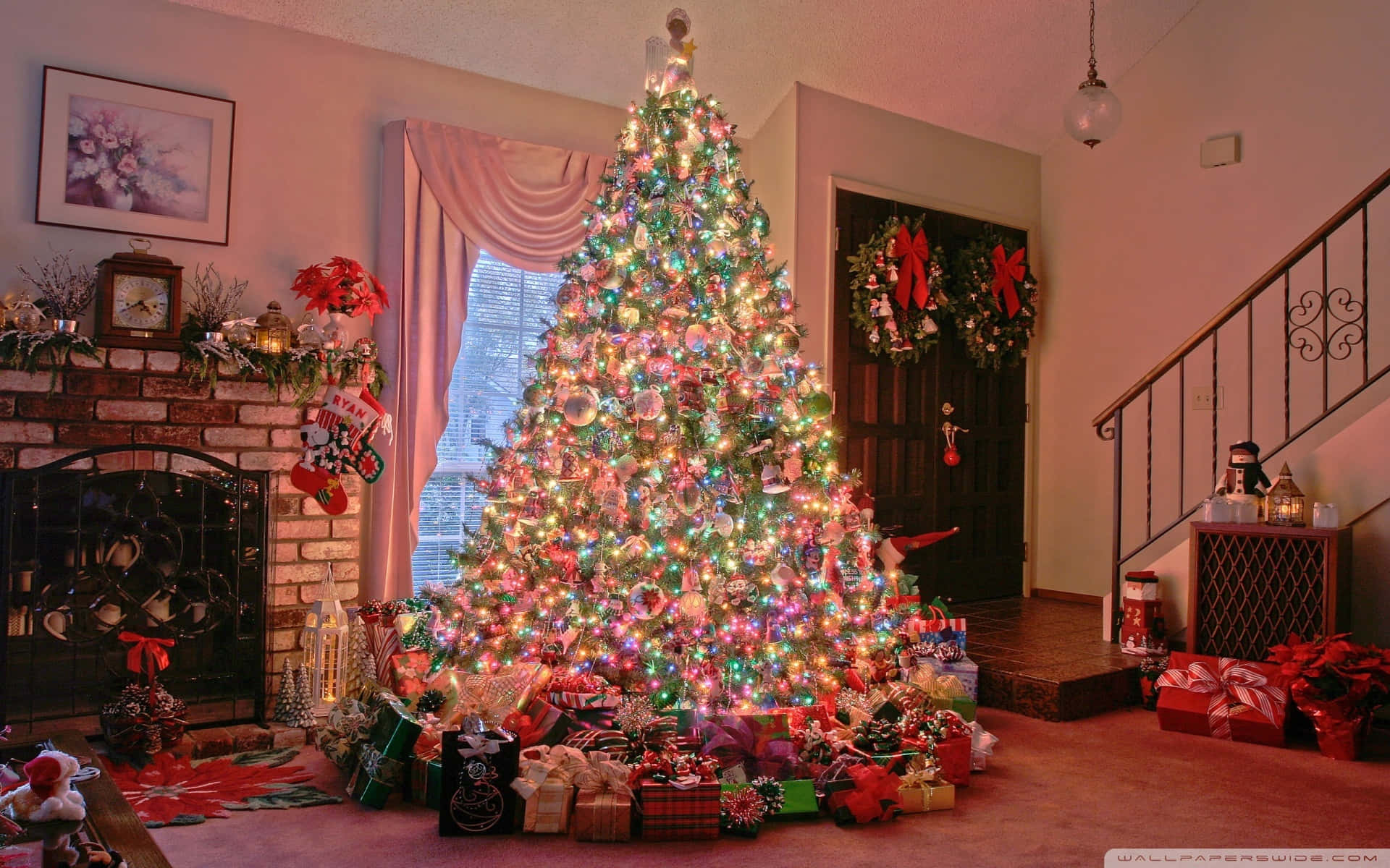 Christmas Village 桌布 壁紙 — 一棵裝飾華麗的聖誕樹，閃爍的燈光和飾品高高聳立在舒適的客廳中，周圍環繞著包裝好的禮物和節日裝飾。
