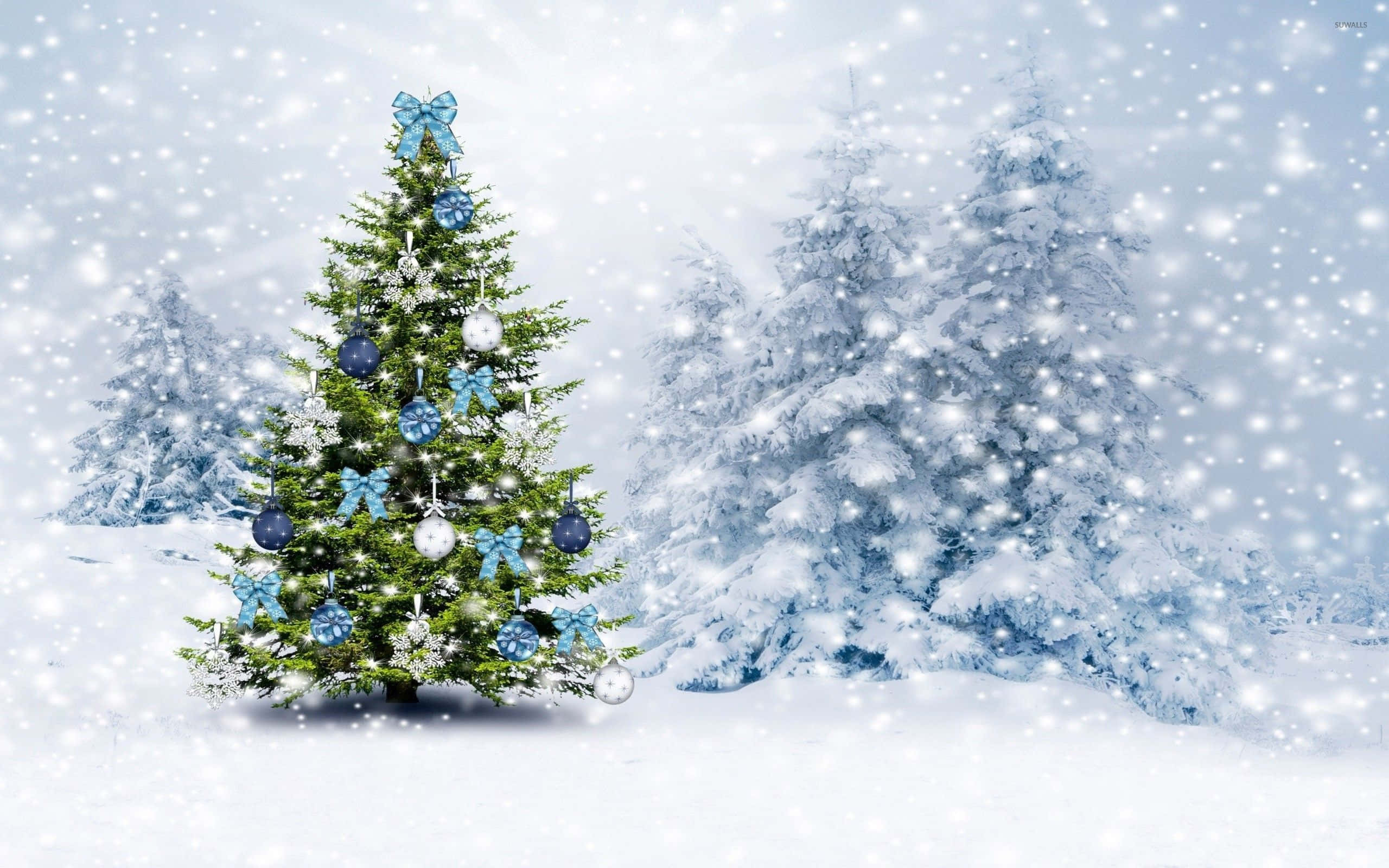 Snowy Christmas 桌布 壁紙 — 一棵裝飾著藍色飾品和蝴蝶結的節日聖誕樹矗立在雪地森林中，雪花輕輕飄落。