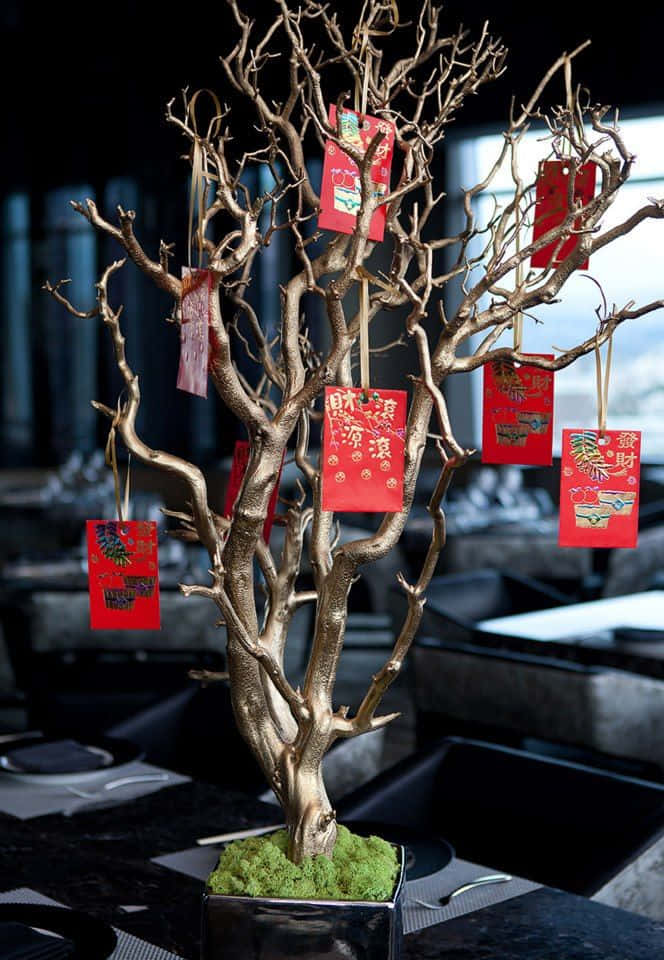 春節 桌布 壁紙 — 一棵金色的光禿樹掛著紅包，懸掛在現代化的飯廳中，背景有模糊的桌椅。