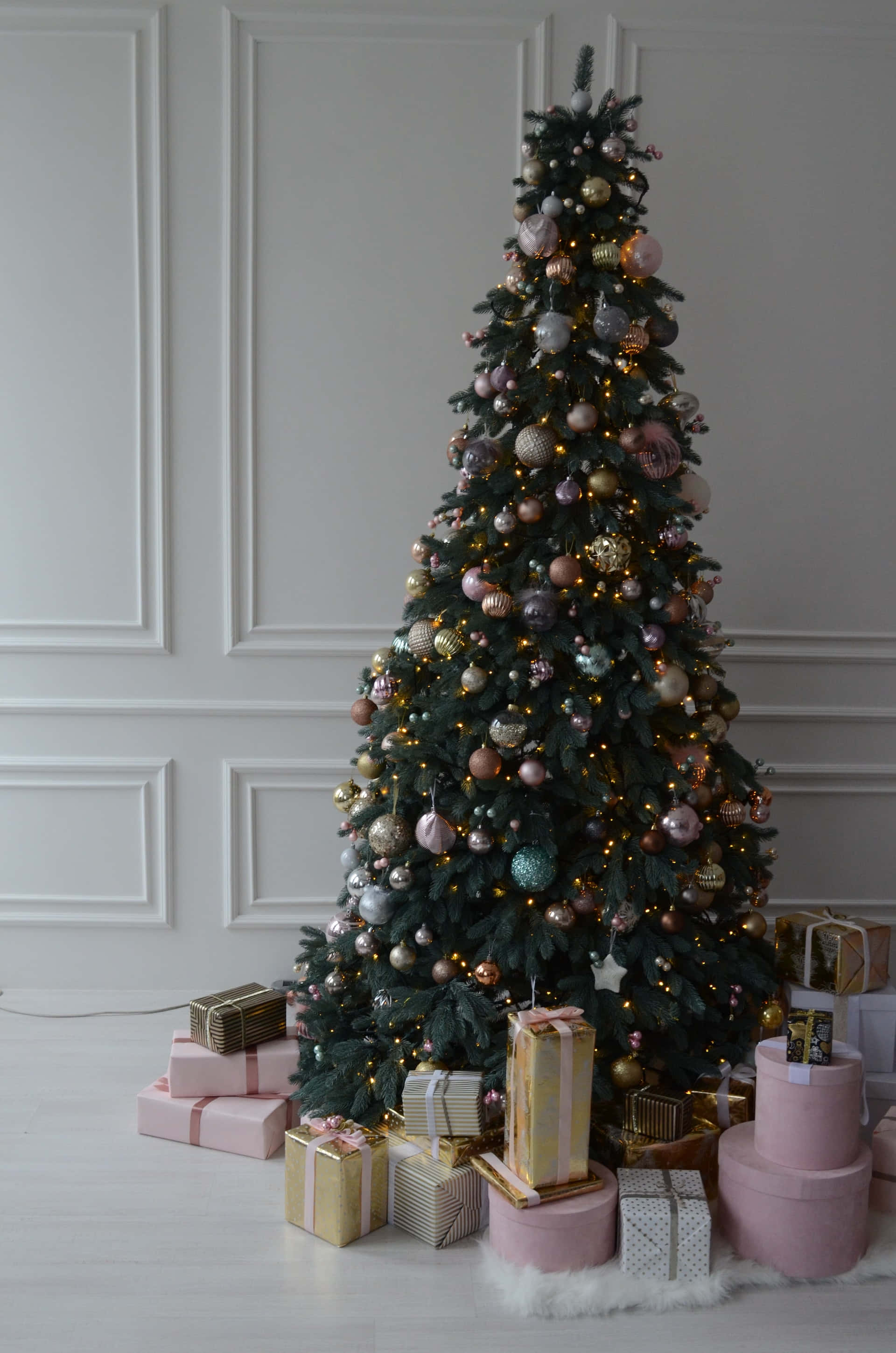 Aesthetic Christmas Tree 桌布 壁紙 — 一棵高大的裝飾聖誕樹，帶有粉紅色、金色和銀色的裝飾品和溫暖的燈光，周圍是淺色木地板上的包裝禮物。