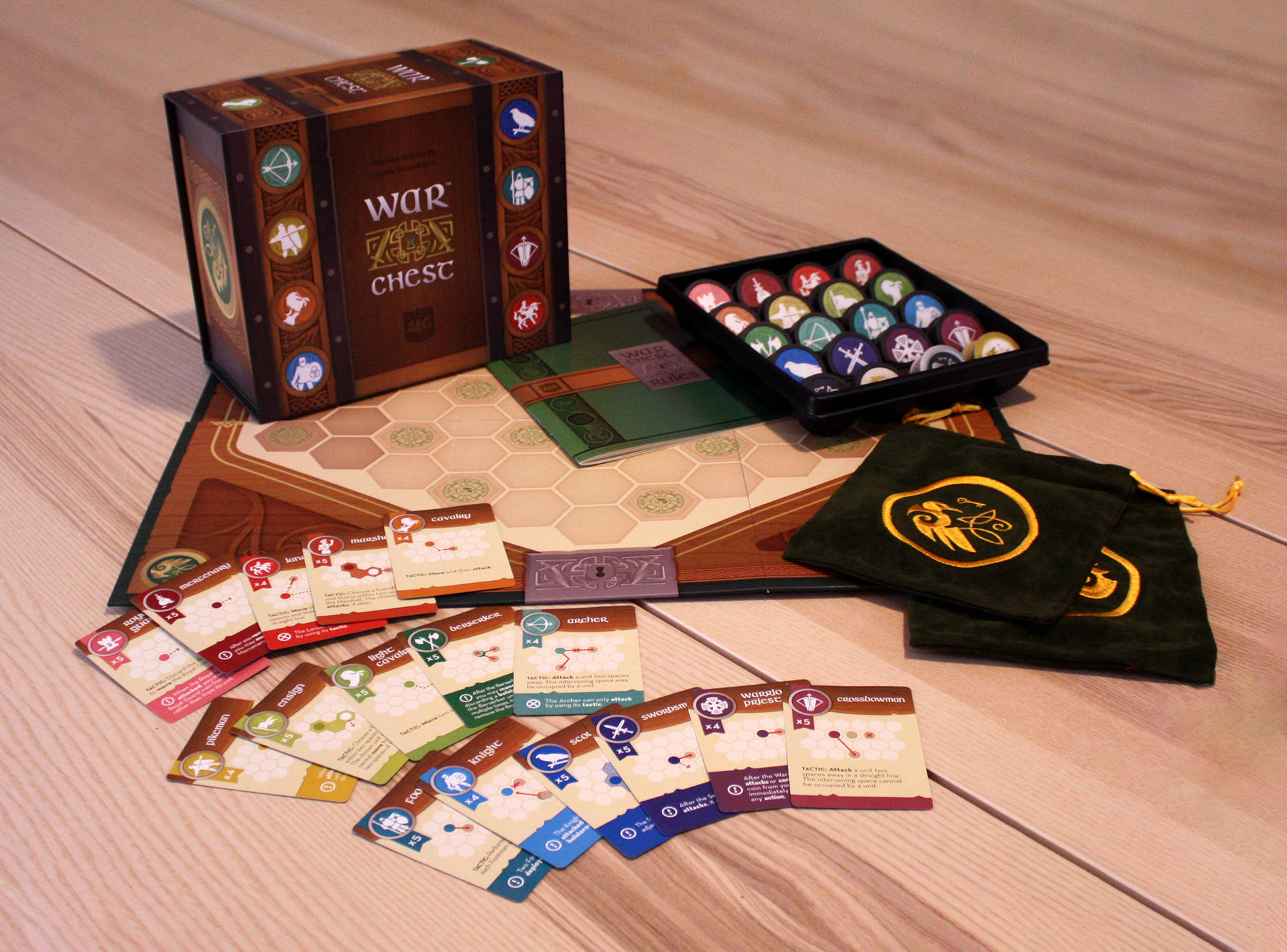 game 桌布 壁紙 — 一款名為 War Chest 的桌上策略遊戲，鋪設在淺色木地板上，附有卡片、籌碼和一個天鵝絨袋。