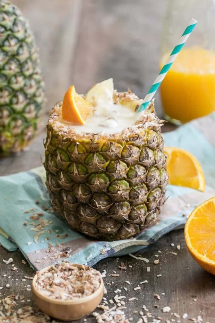 Pineapple 桌布 壁紙 — 一款奶油狀的熱帶飲品，盛載於新鮮鳳梨中，搭配柳橙片和條紋吸管，置於質樸的木桌上。