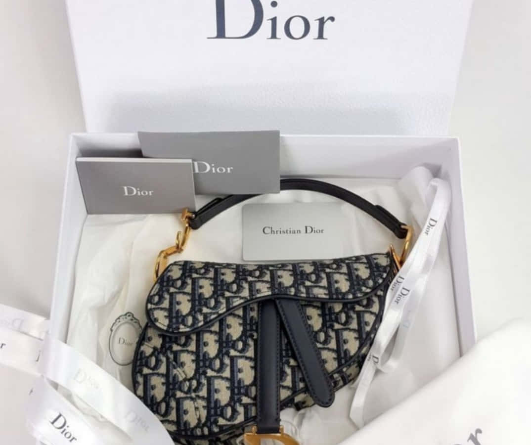 Dior 動態 桌布 壁紙 — 一款帶有字母組合圖案的Dior馬鞍袋優雅地放置在品牌白色盒子中，內襯薄紙和標籤。
