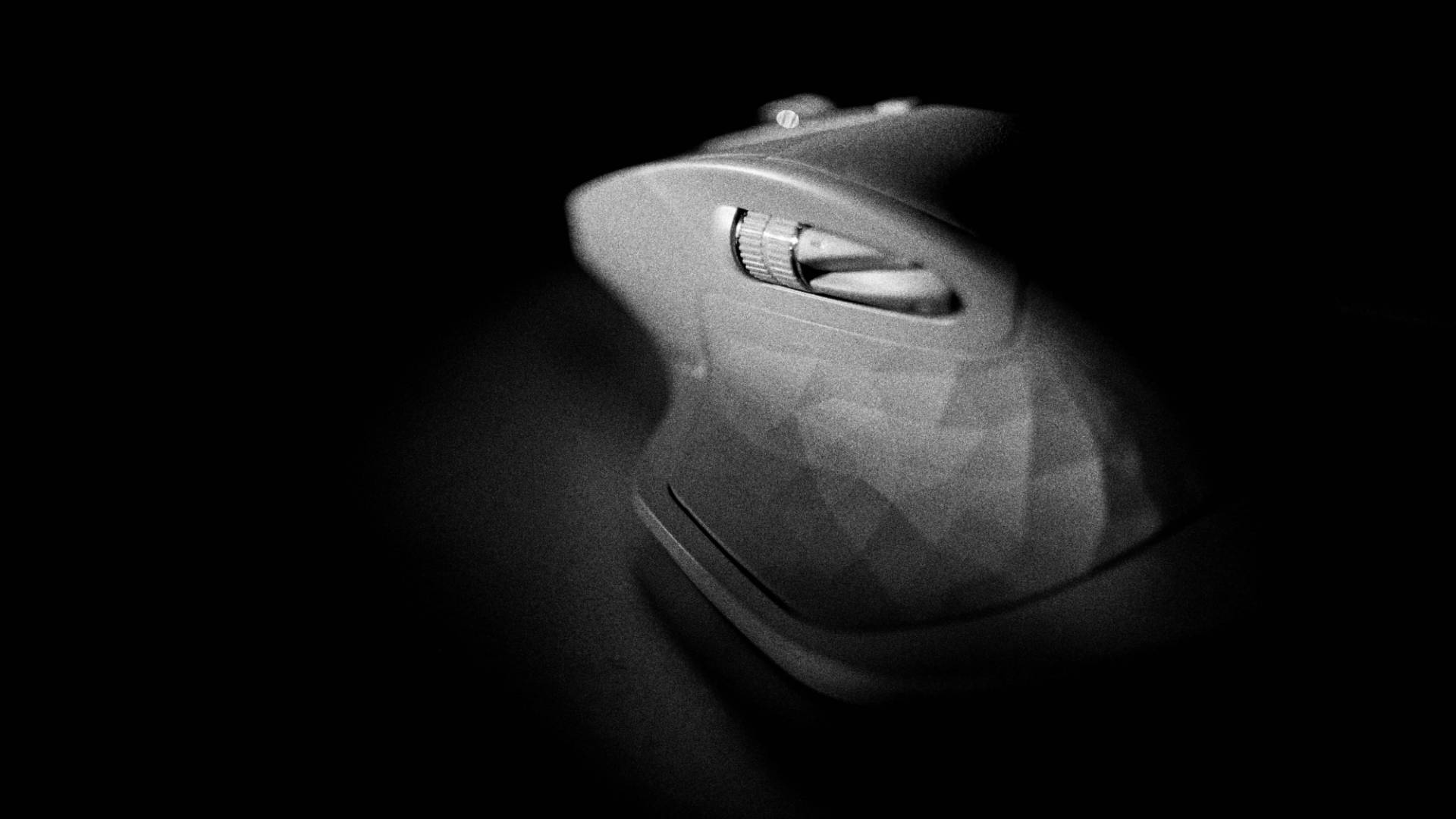 Logitech 桌布 壁紙 — 一款時尚的人體工學電腦滑鼠，在漆黑背景下被戲劇性的聚光燈照亮。