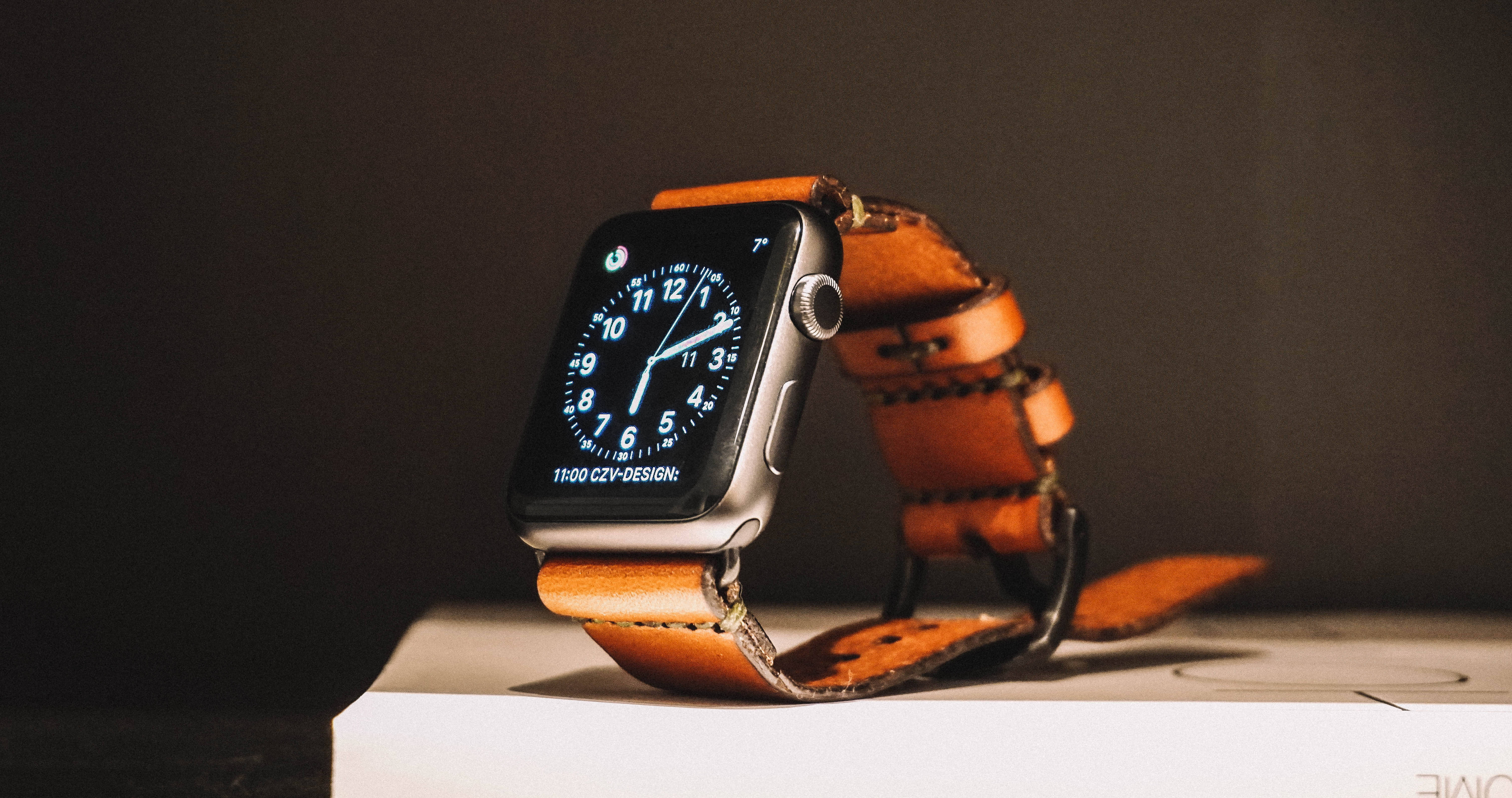 Apple Watch 動態 桌布 壁紙 — 一款時尚的智慧手錶搭配棕色皮革錶帶，放在白色盒子上，背景為深色。