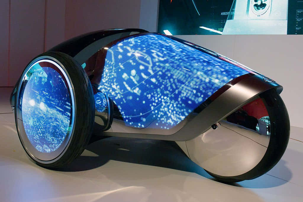 Car Technology 桌布 壁紙 — 一款時尚的未來主義車輛，其彎曲車身和車輪上帶有發光的藍色數位圖案，在現代展覽空間中展示。