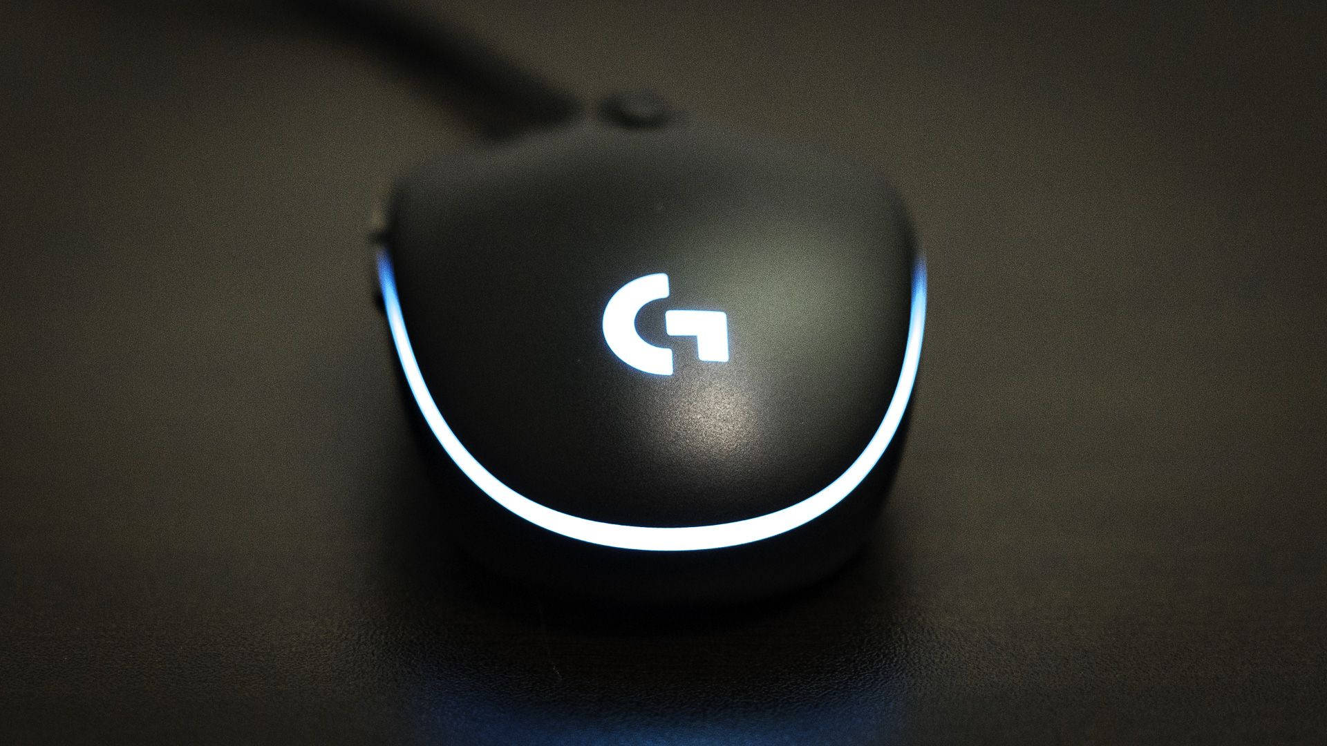 羅技 桌布 壁紙 — 一款時尚的黑色 Logitech 遊戲滑鼠，帶有發光的白色標誌和重點燈，放置在深色紋理表面上。