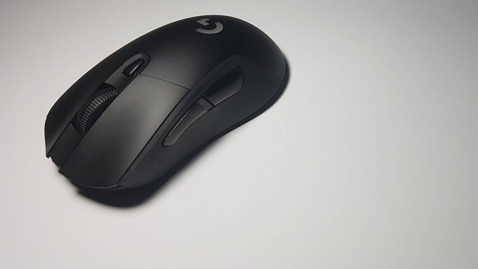 羅技 桌布 壁紙 — 一款時尚的黑色Logitech遊戲滑鼠放置在帶有柔和陰影的純白表面上。