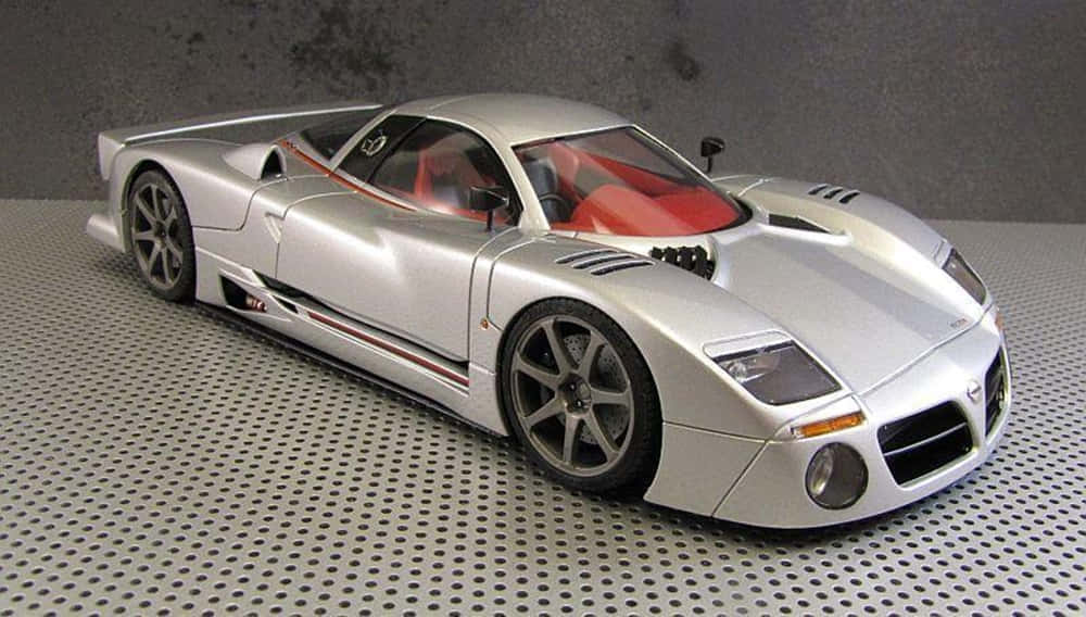 Car Model 桌布 壁紙 — 一款流線型銀色跑車模型，紅色內裝，放置在穿孔金屬表面上，背景為灰色牆壁。