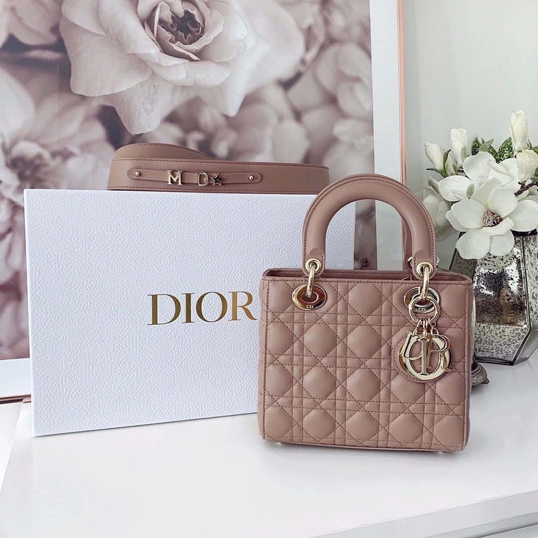 Dior 動態 桌布 壁紙 — 一款粉紅色Dior Lady Dior手提包，搭配金色金屬配件，優雅地放在其品牌盒子和白色花朵旁邊，置於潔白表面上。
