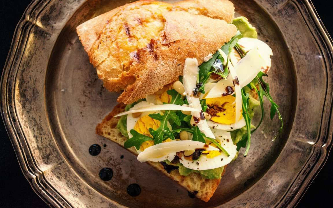 Egg 桌布 壁紙 — 一款美食開放式三明治，配上酪梨、水煮蛋和芝麻葉，放在一個暗淡的銀盤上。