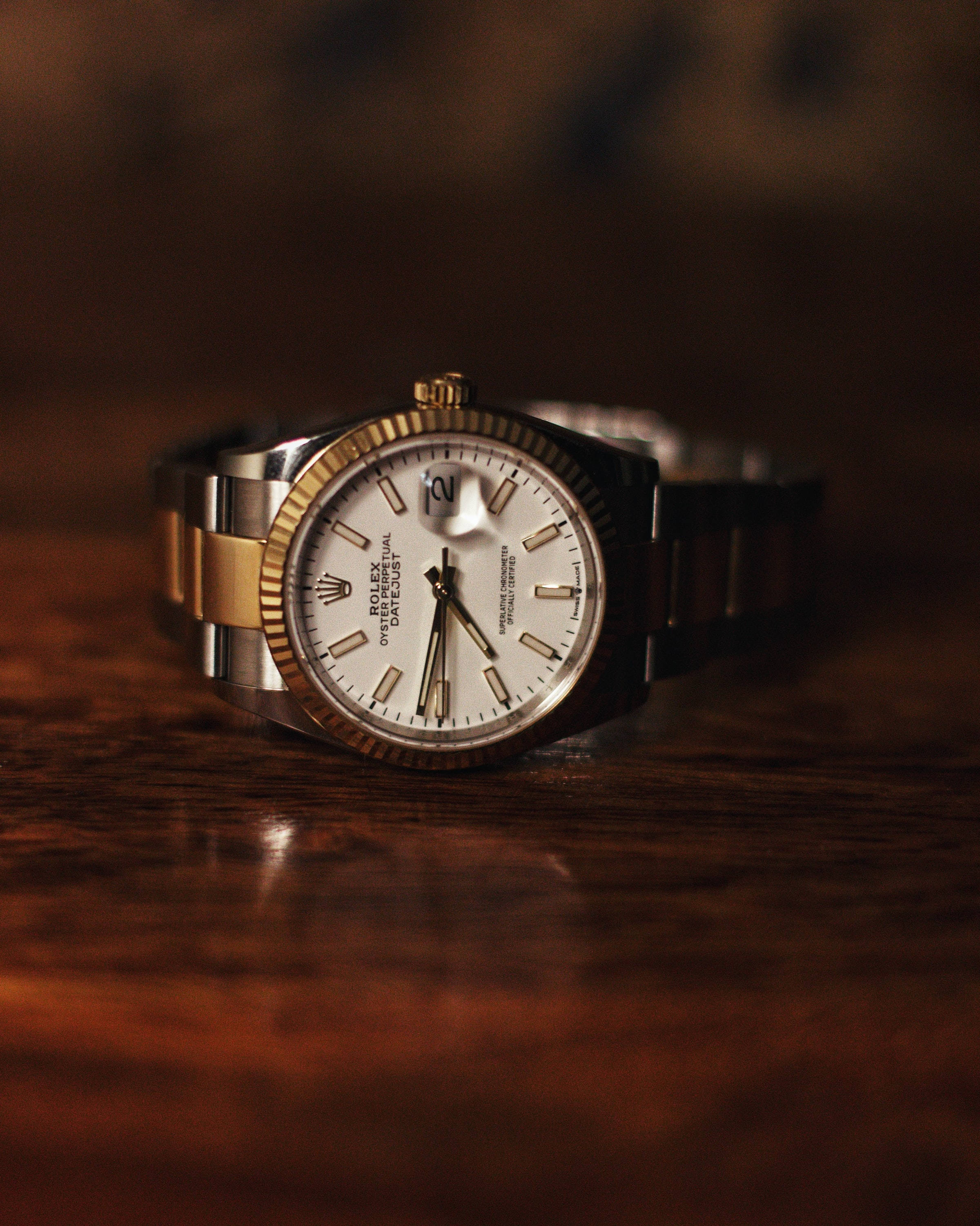 復古 桌布 壁紙 — 一款豪華的勞力士 Oyster Perpetual Datejust 手錶，配備金鋼錶帶，在溫暖的環境燈光下優雅地放置在豐富的木質表面上。