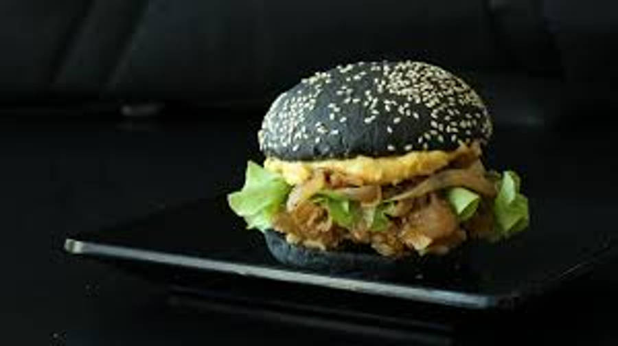 Burger King 桌布 壁紙 — 一款黑芝麻籽美食漢堡，搭配脆皮培根、生菜和醬汁，優雅地擺放在深色背景下的時尚黑色餐盤上。