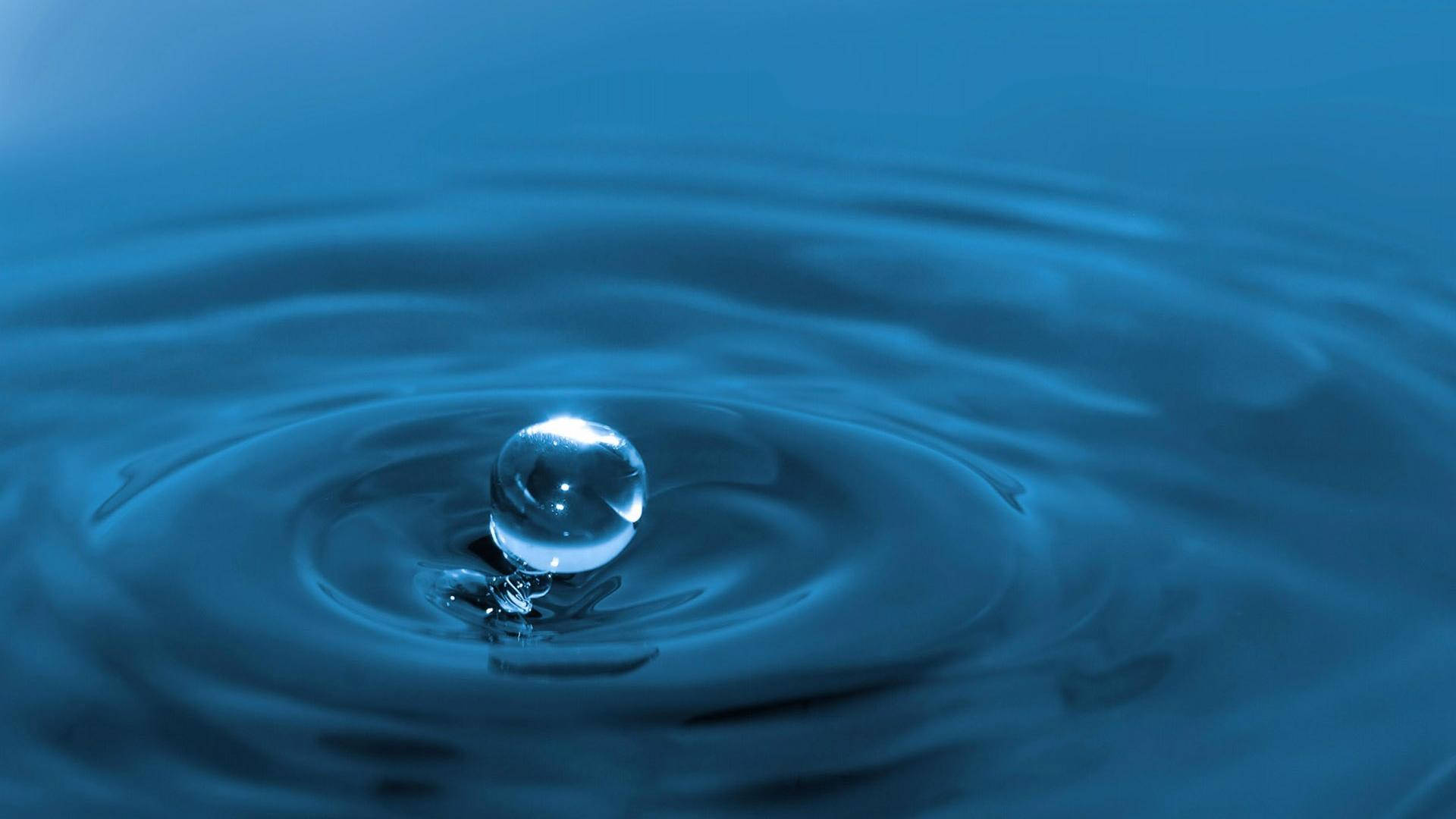 水 桌布 壁紙 — 一滴完美如玻璃的水滴懸浮在藍色水池上方，以慢動作產生同心漣漪。